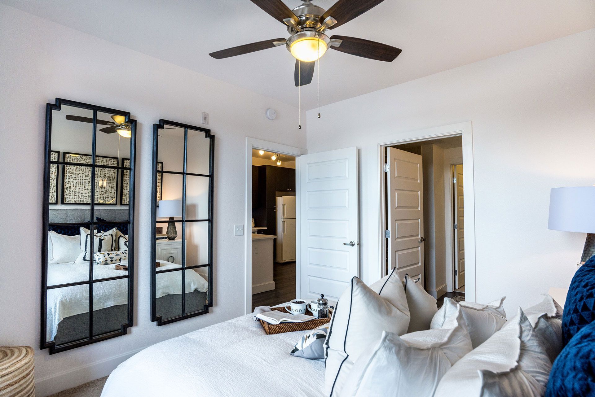 Bright bedroom with a ceiling fan, two grid-framed mirrors, and a doorway to the kitchen.