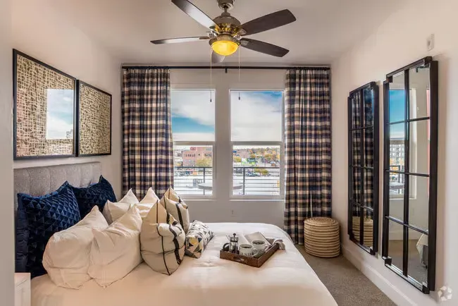 Bedroom with bed, pillows, patterned curtains, windows, and two decorative mirrors.