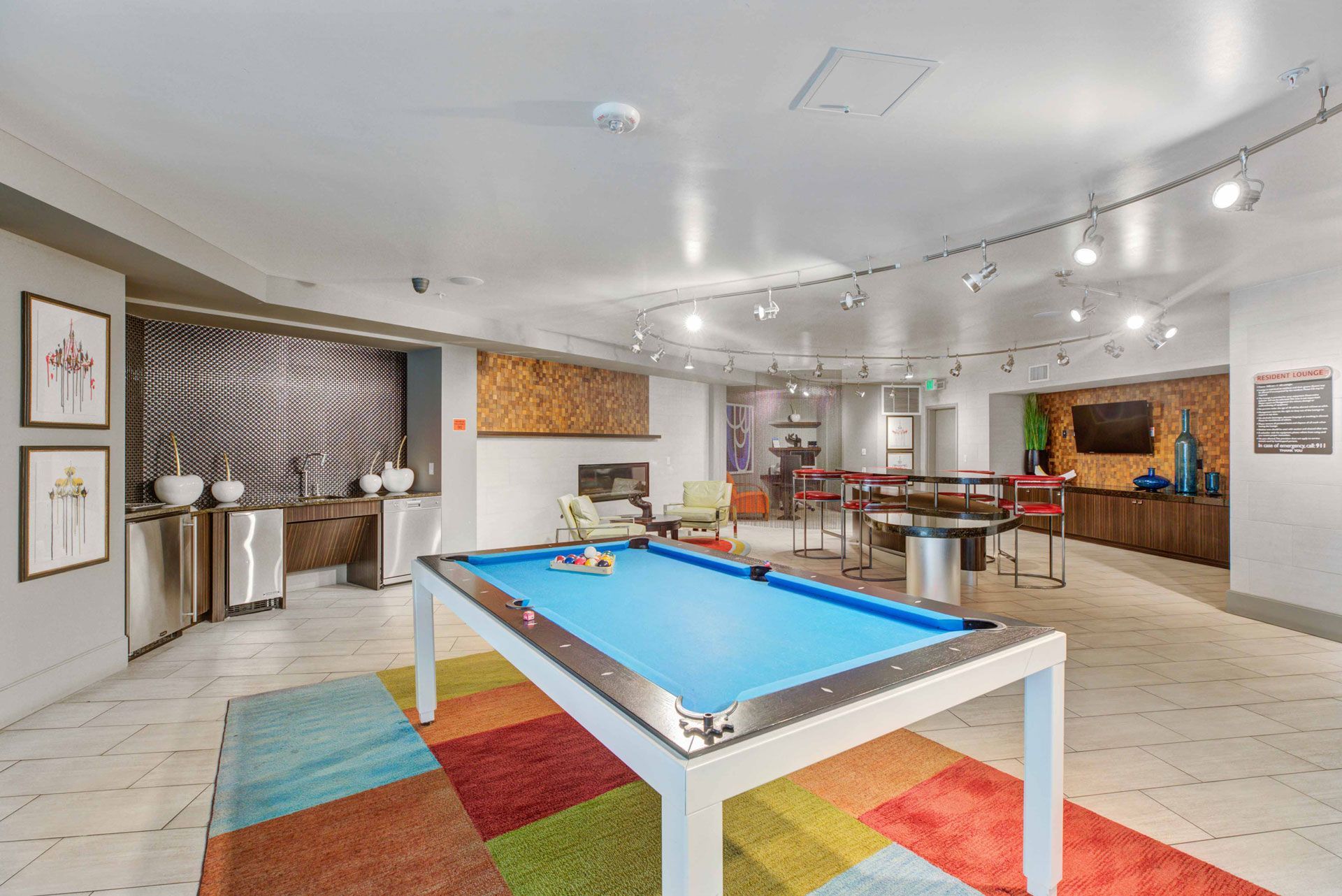 A recreation room with a pool table on a colorful rug. Seating, artwork, and lighting complete the space.