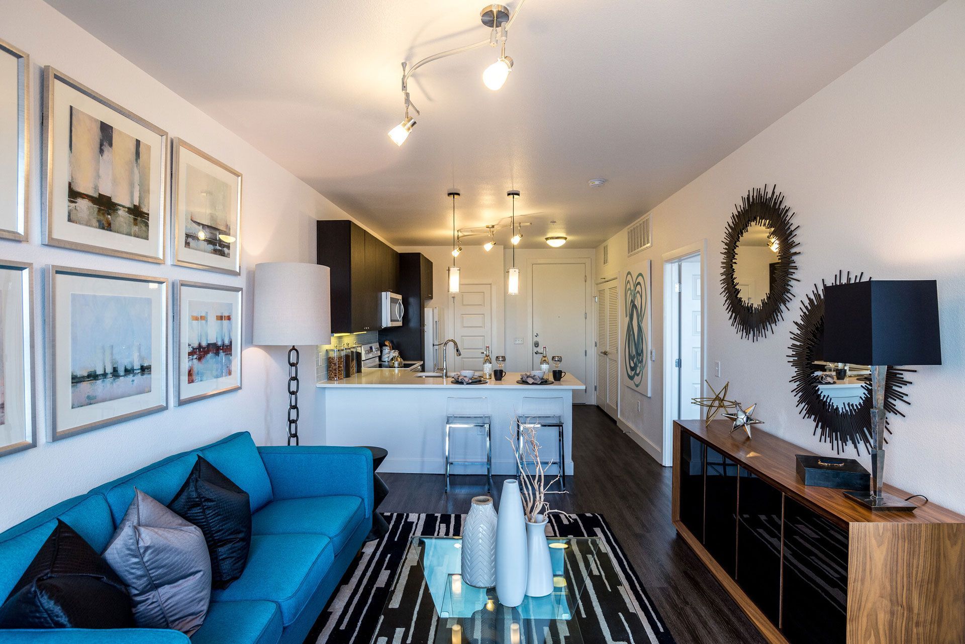 Open-plan living area with a blue sofa, glass coffee table, and a modern kitchen island.