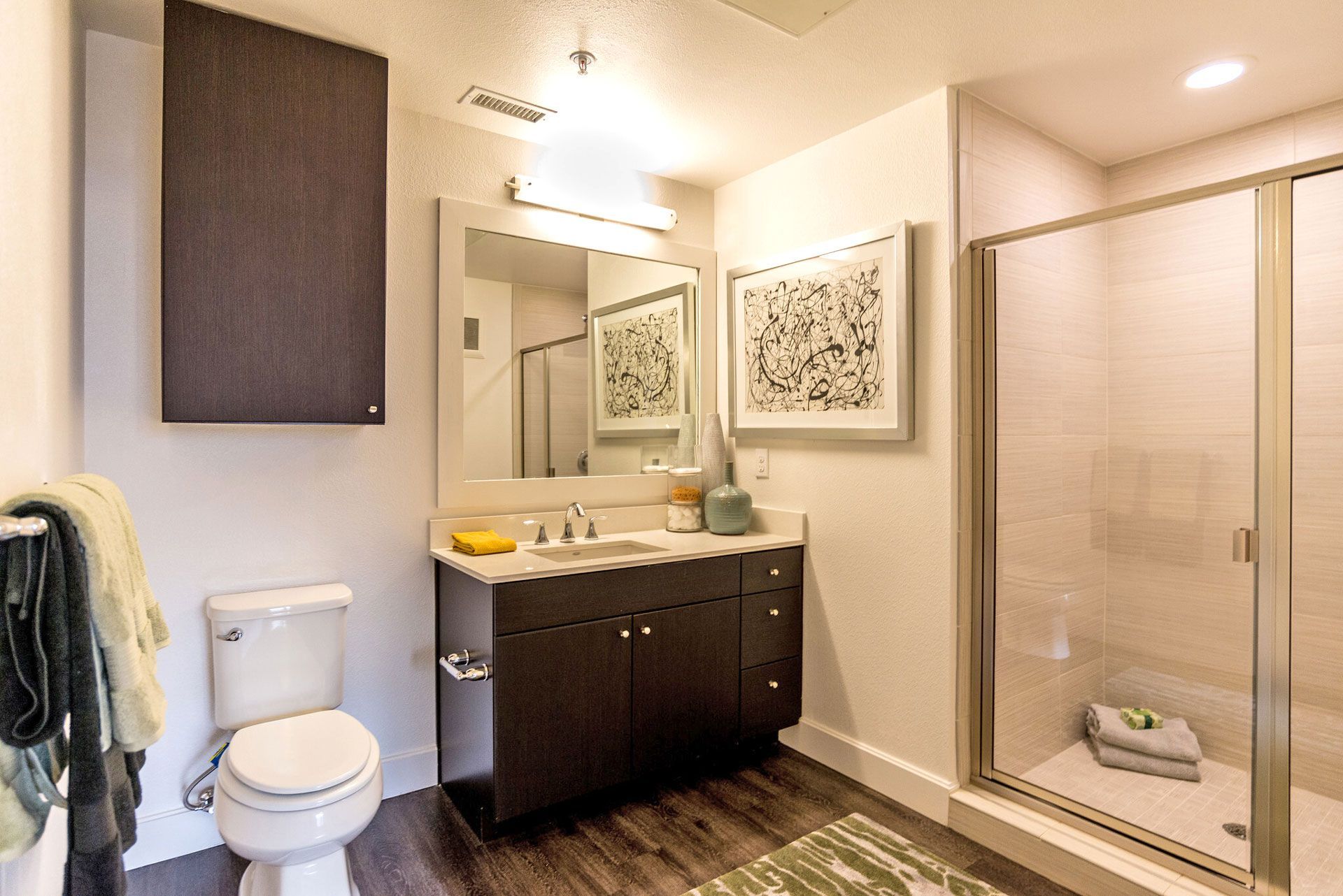 Bathroom with dark wood vanity, large mirror, framed art, glass shower, and toilet.