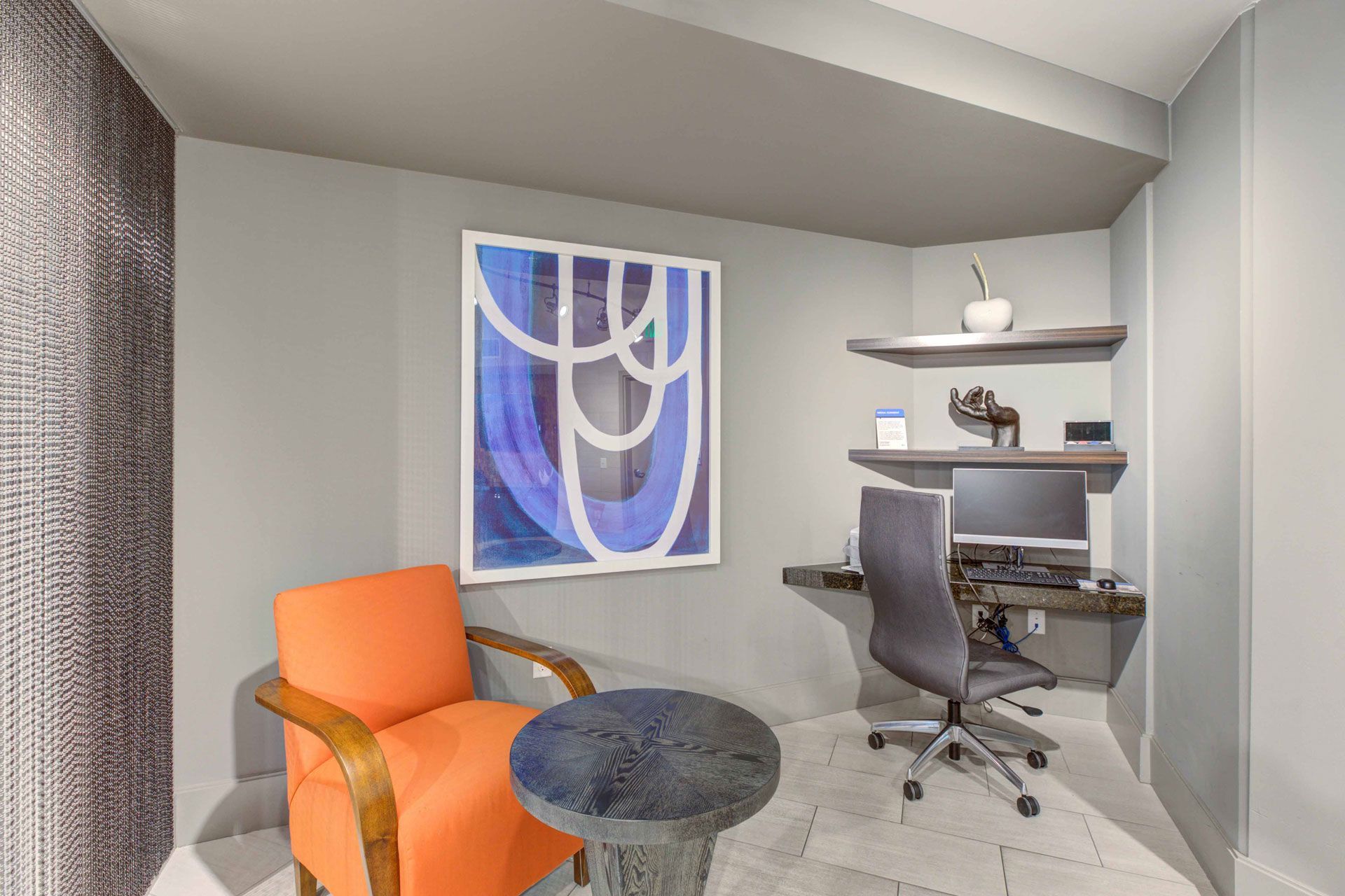 Interior view of a compact apartment study area with a desk, computer monitor, and orange chair.