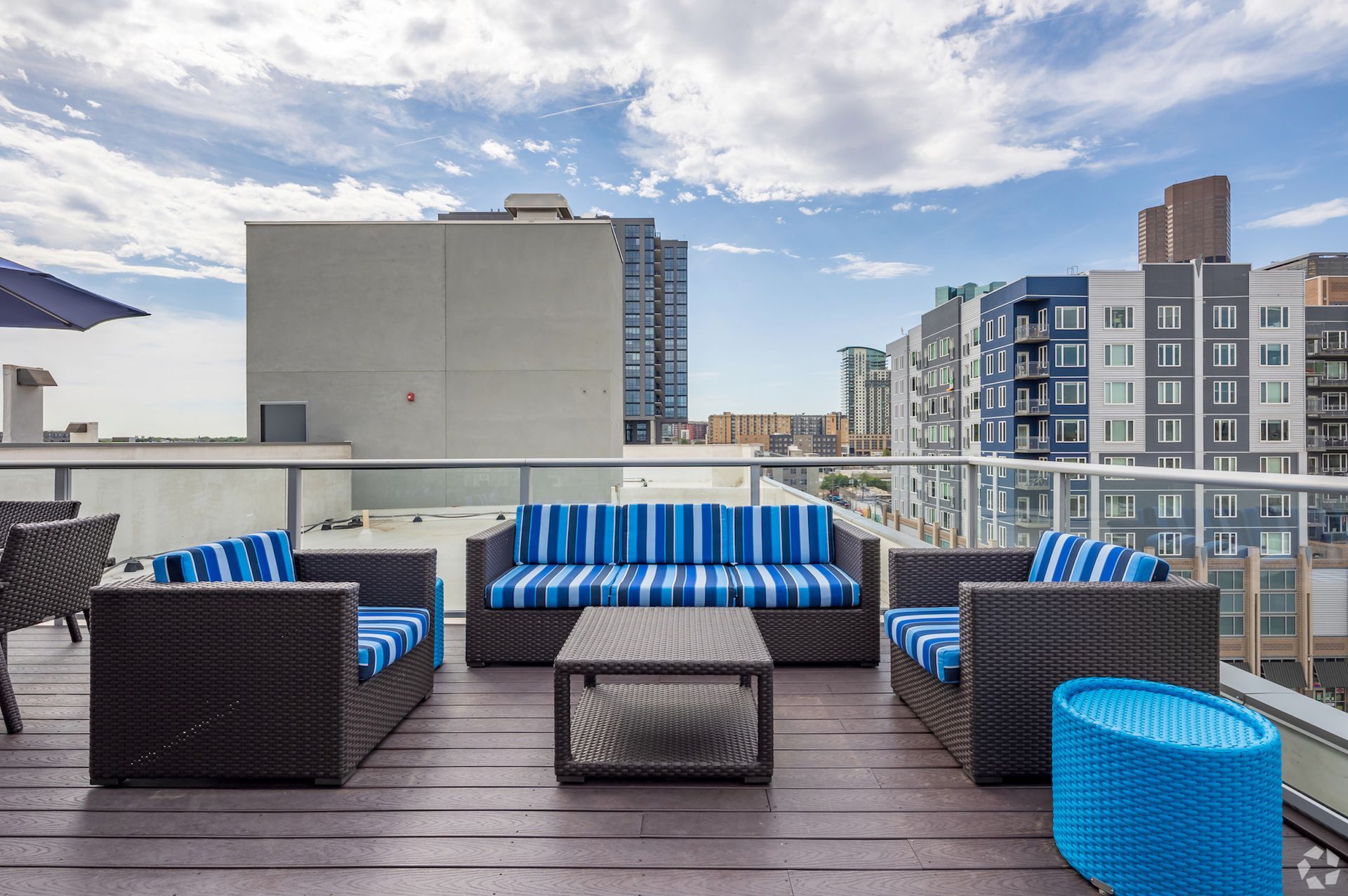 Rooftop terrace with wicker seating and blue-striped cushions overlooking city skyline.
