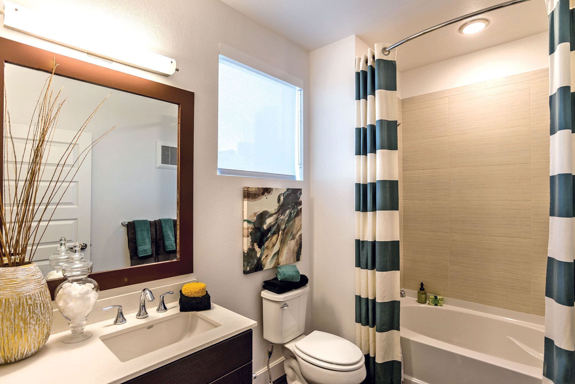 Bathroom in a modern apartment with sink, mirror, toilet, tub, and teal/white striped shower curtain.