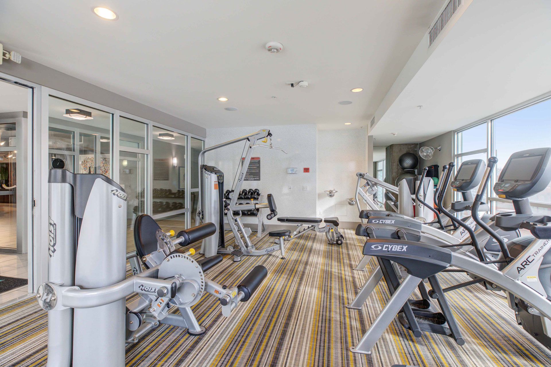Interior fitness center with cardio machines, weight machines, and large windows.