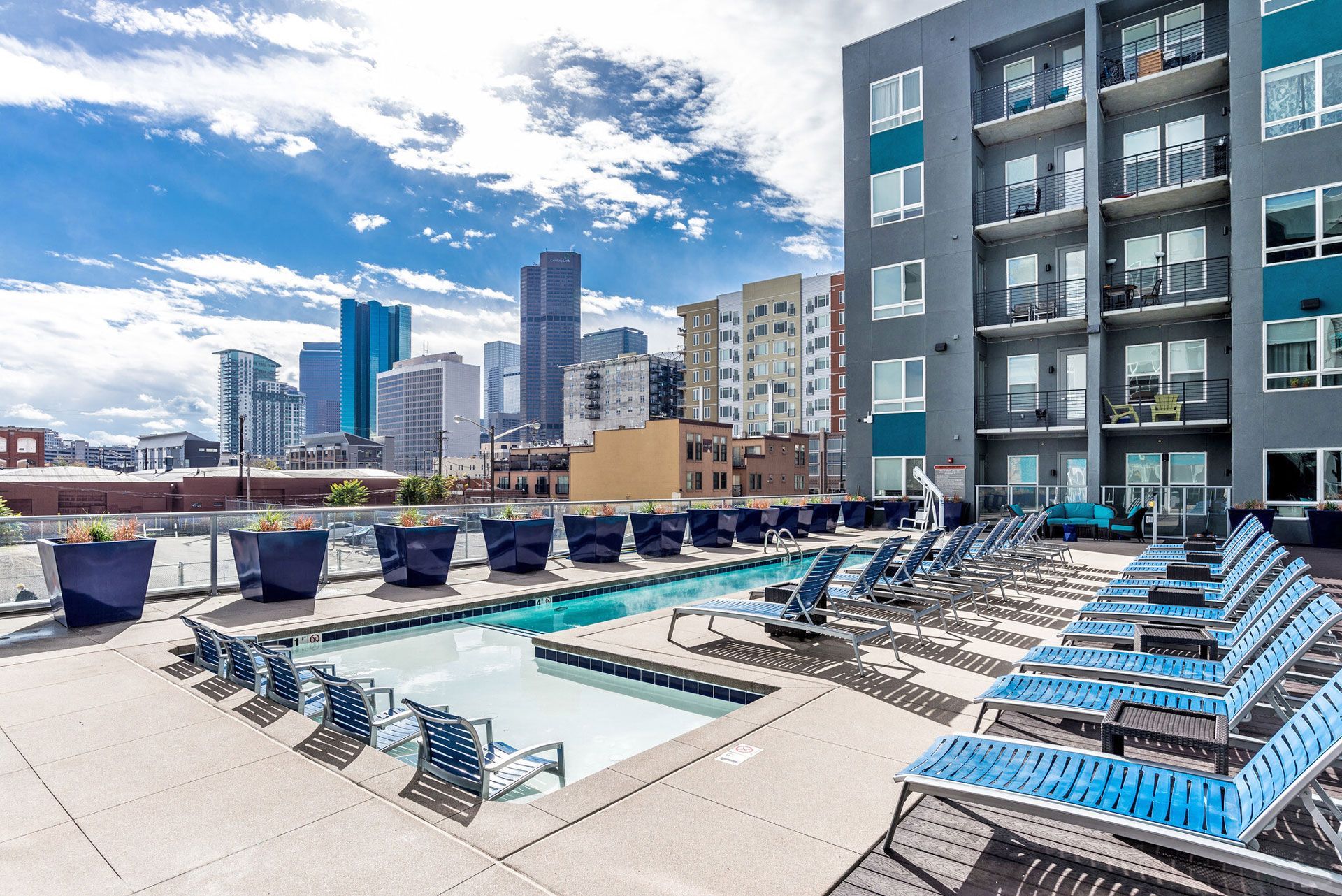 Rooftop pool deck with blue lounge chairs and city skyline.