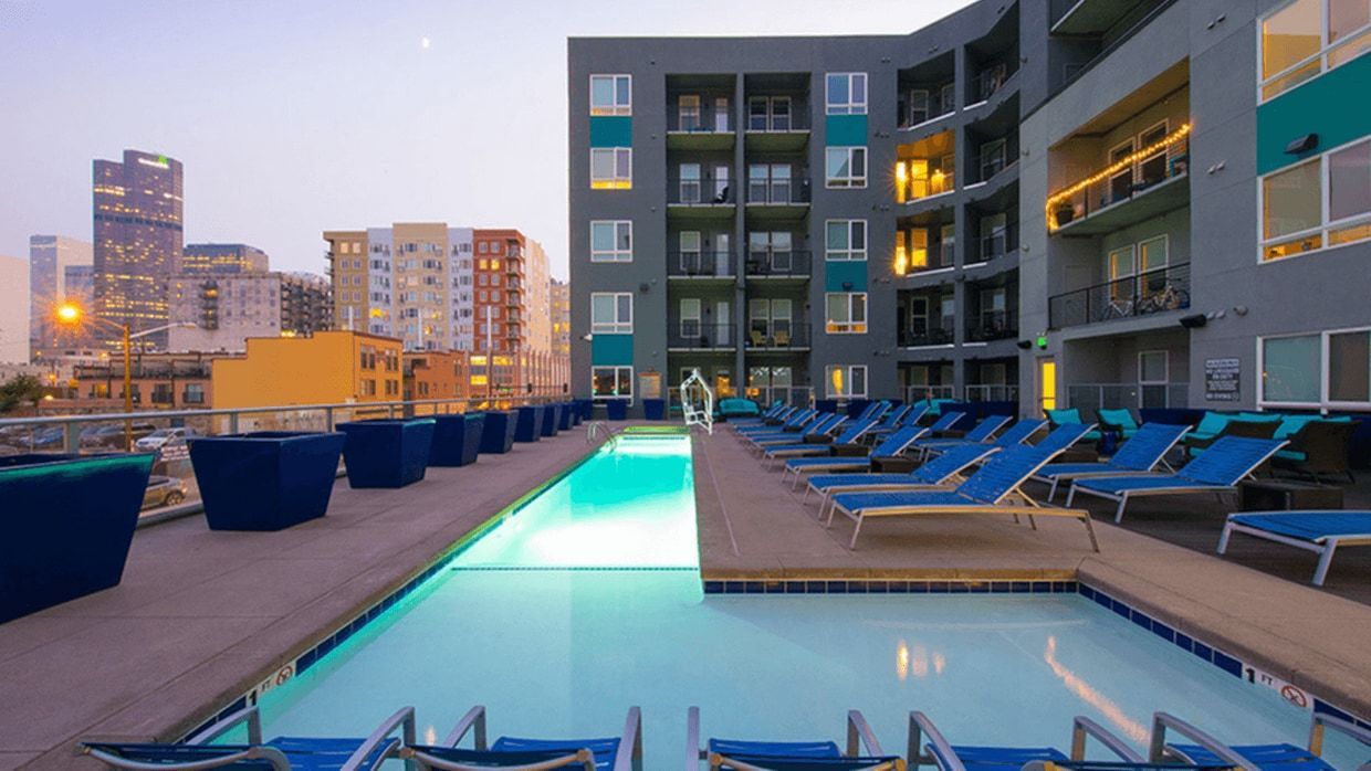 Rooftop pool with lounge chairs at dusk, overlooking city skyline. Gray and teal building.