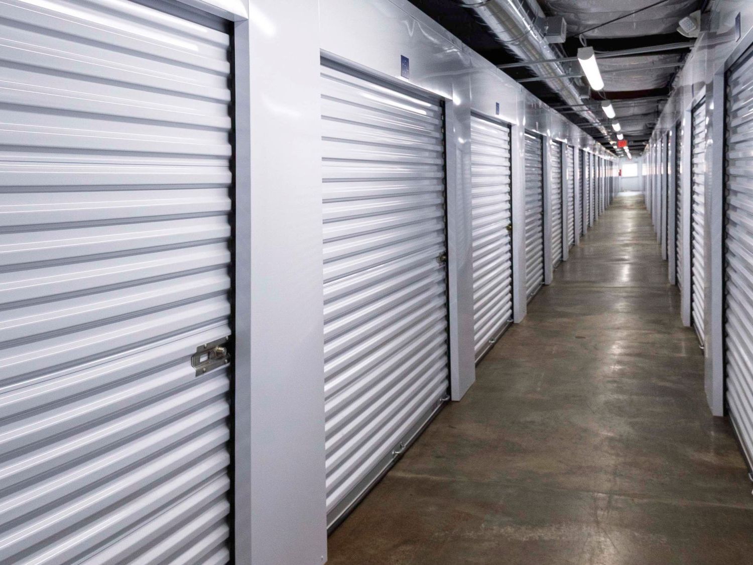 A hallway with climate controlled self-storage units with white doors that is monitored by security cameras.