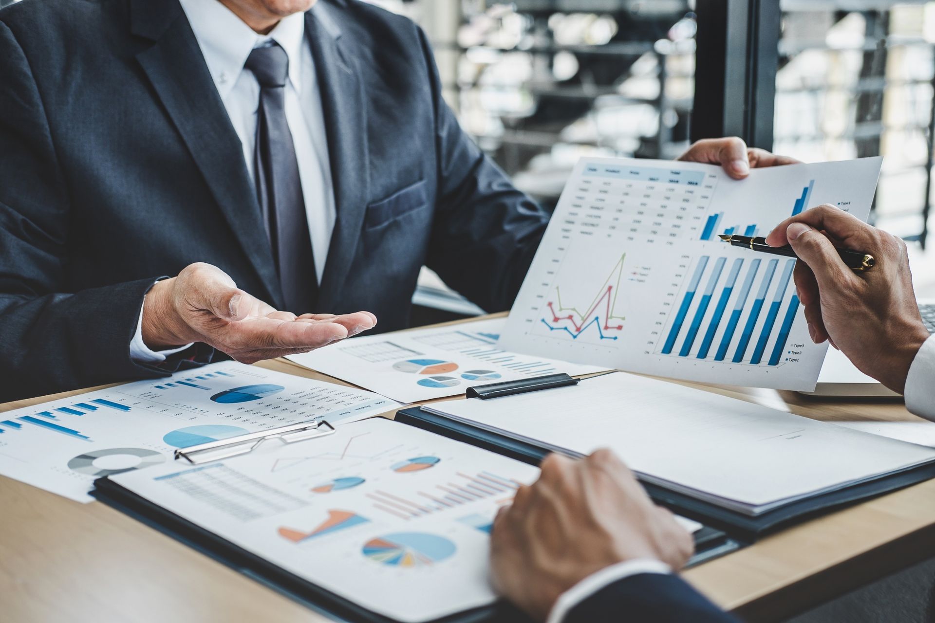 Two business professionals review charts and data reports on a desk during a professional meeting.