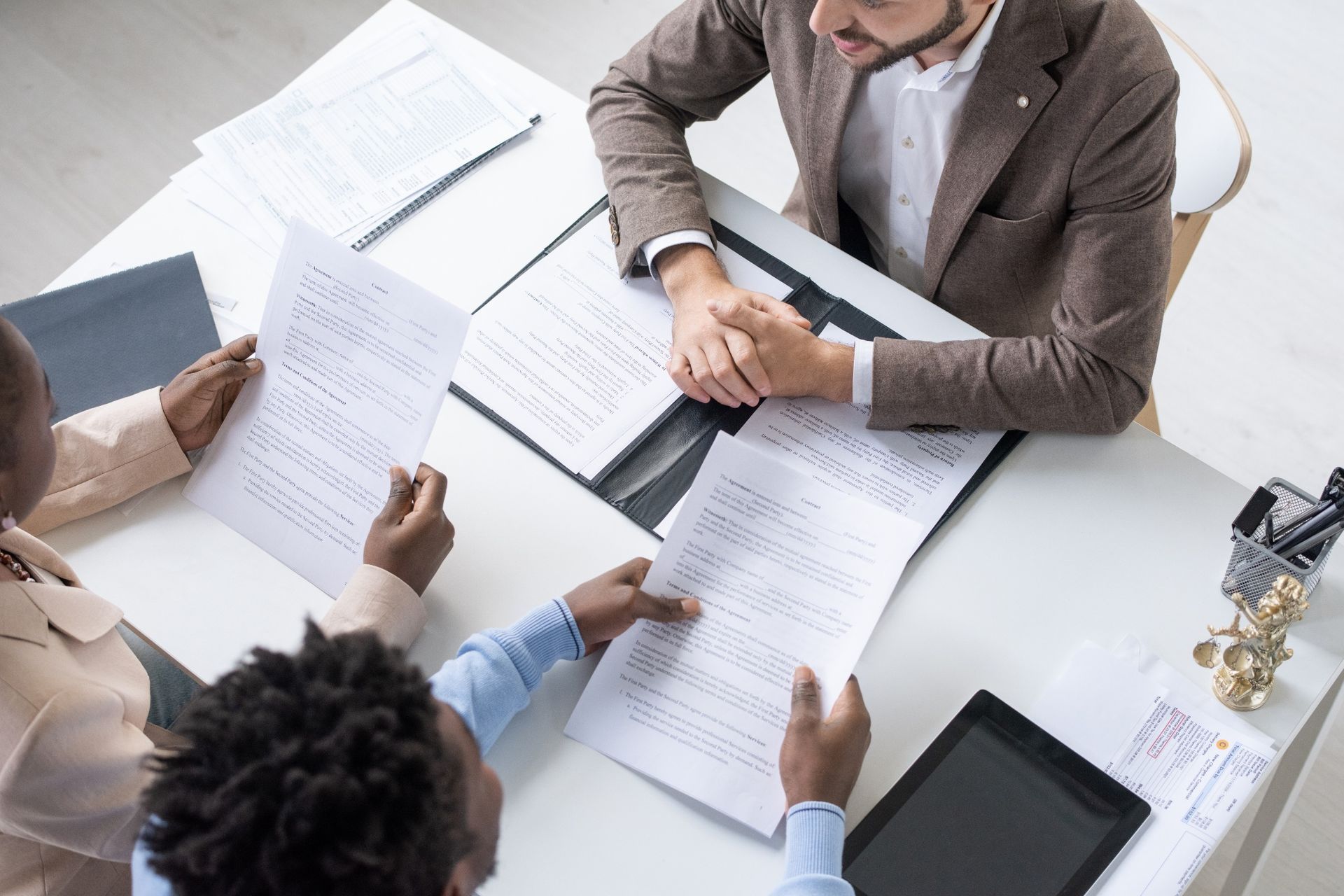Three people sit at a table reviewing documents during a meeting in a bright office.