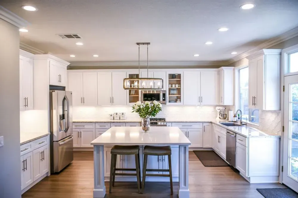 White modern kitchen with island, cabinets, stainless steel appliances, and hardwood floors.