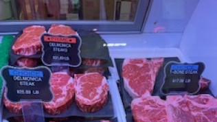 Meat display case with Delmonico and T-bone steaks; price tags indicate cost per pound.