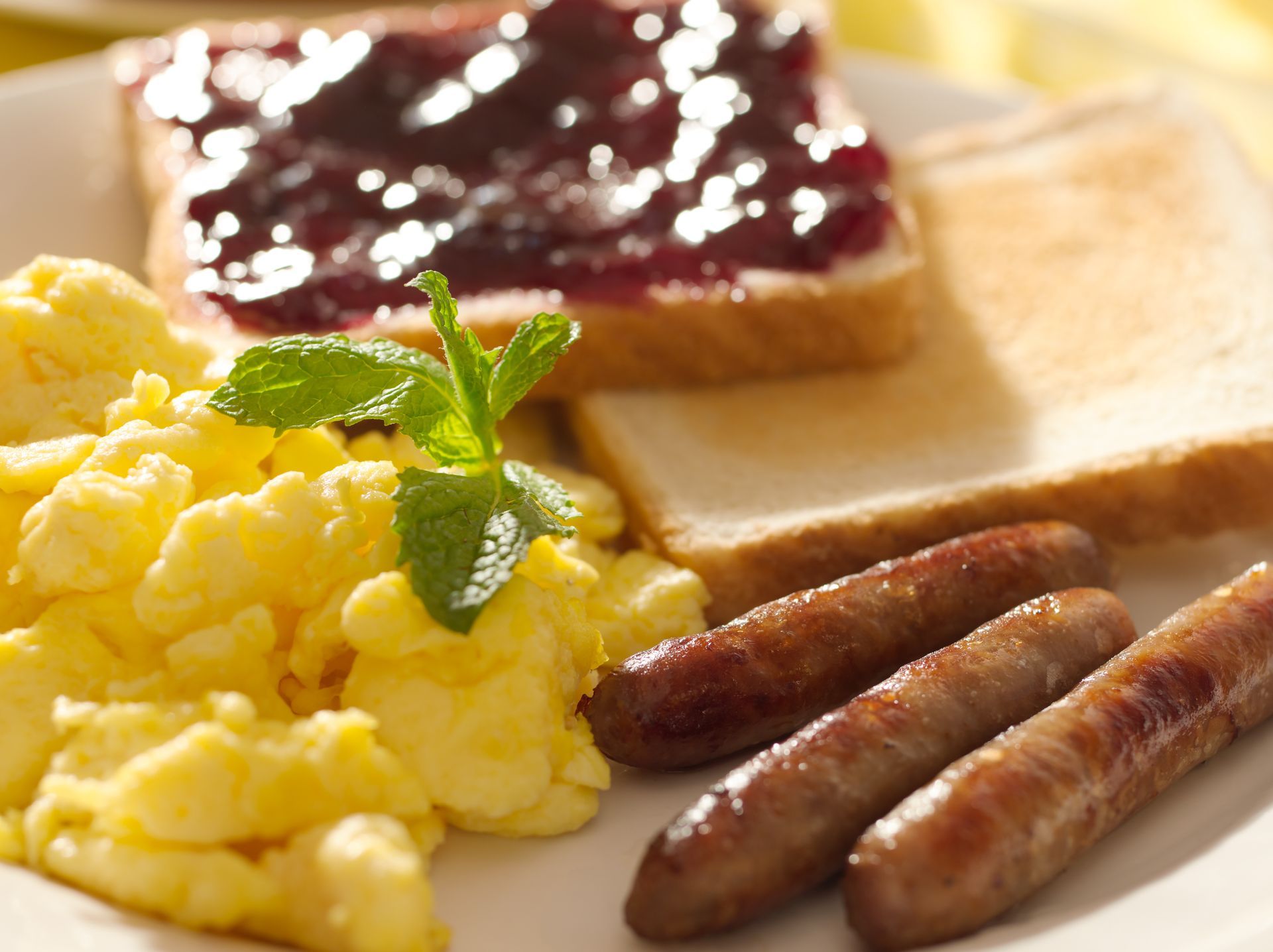 Breakfast plate with scrambled eggs, toast with jam, and sausages.
