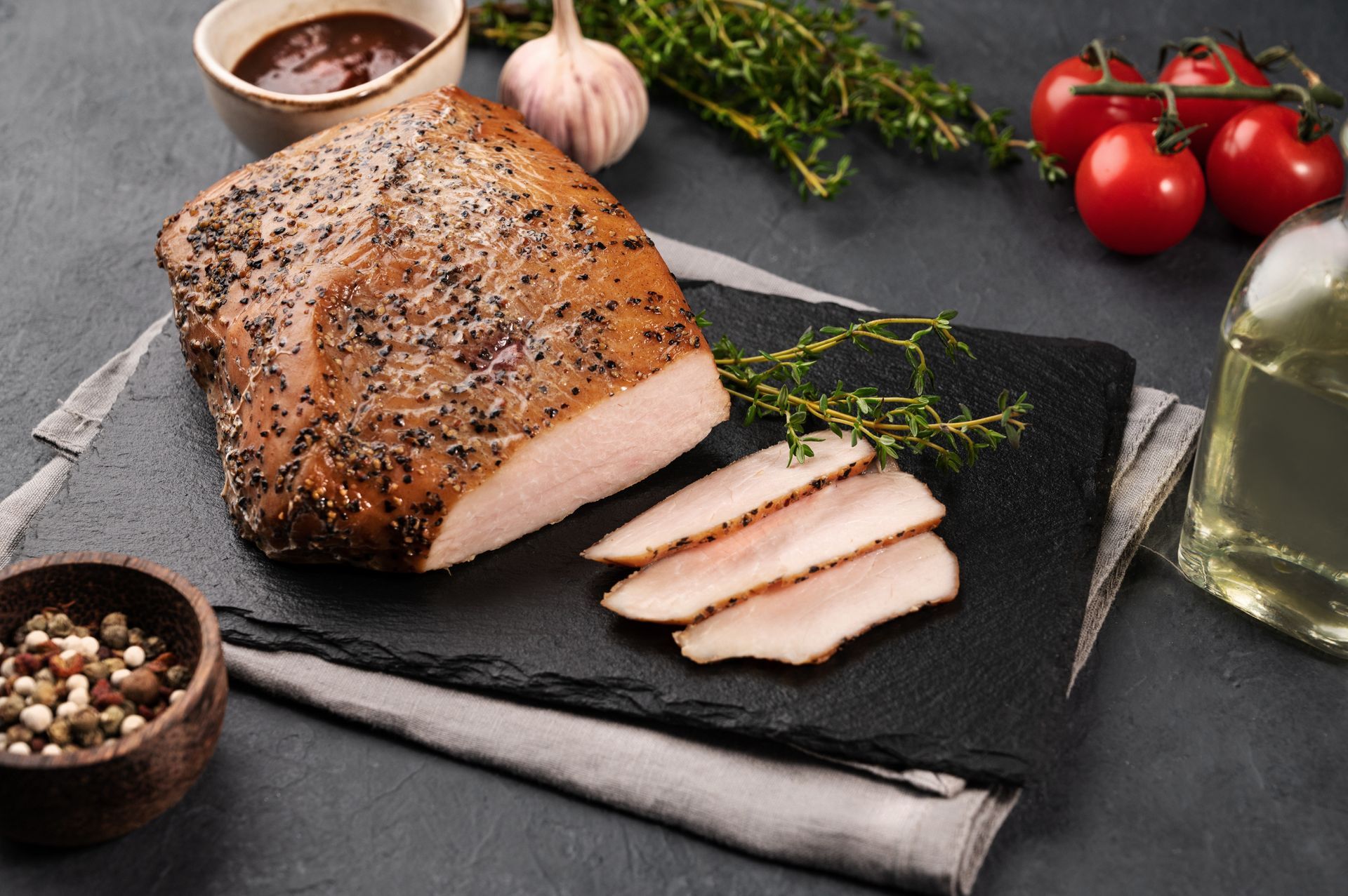 Smoked meat with sliced portions on a slate with thyme, garlic, tomatoes, and peppercorns. Smoked meat with sliced portions on a slate with thyme, garlic, tomatoes, and peppercorns.