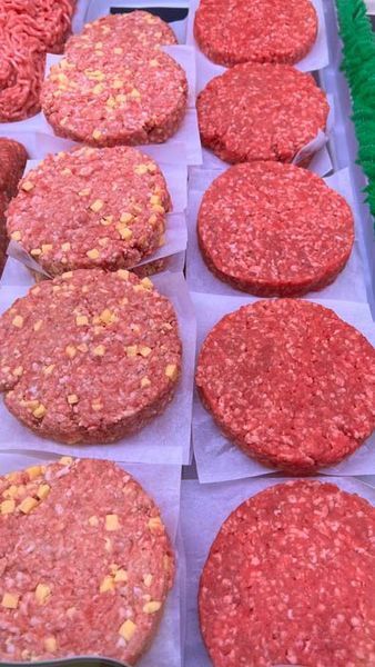 Raw hamburger patties on display in a butcher shop, some with visible yellow seasoning.