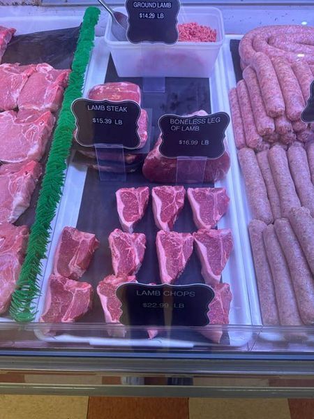 Meat display in a butcher shop. Includes various cuts of lamb and sausage with price labels.