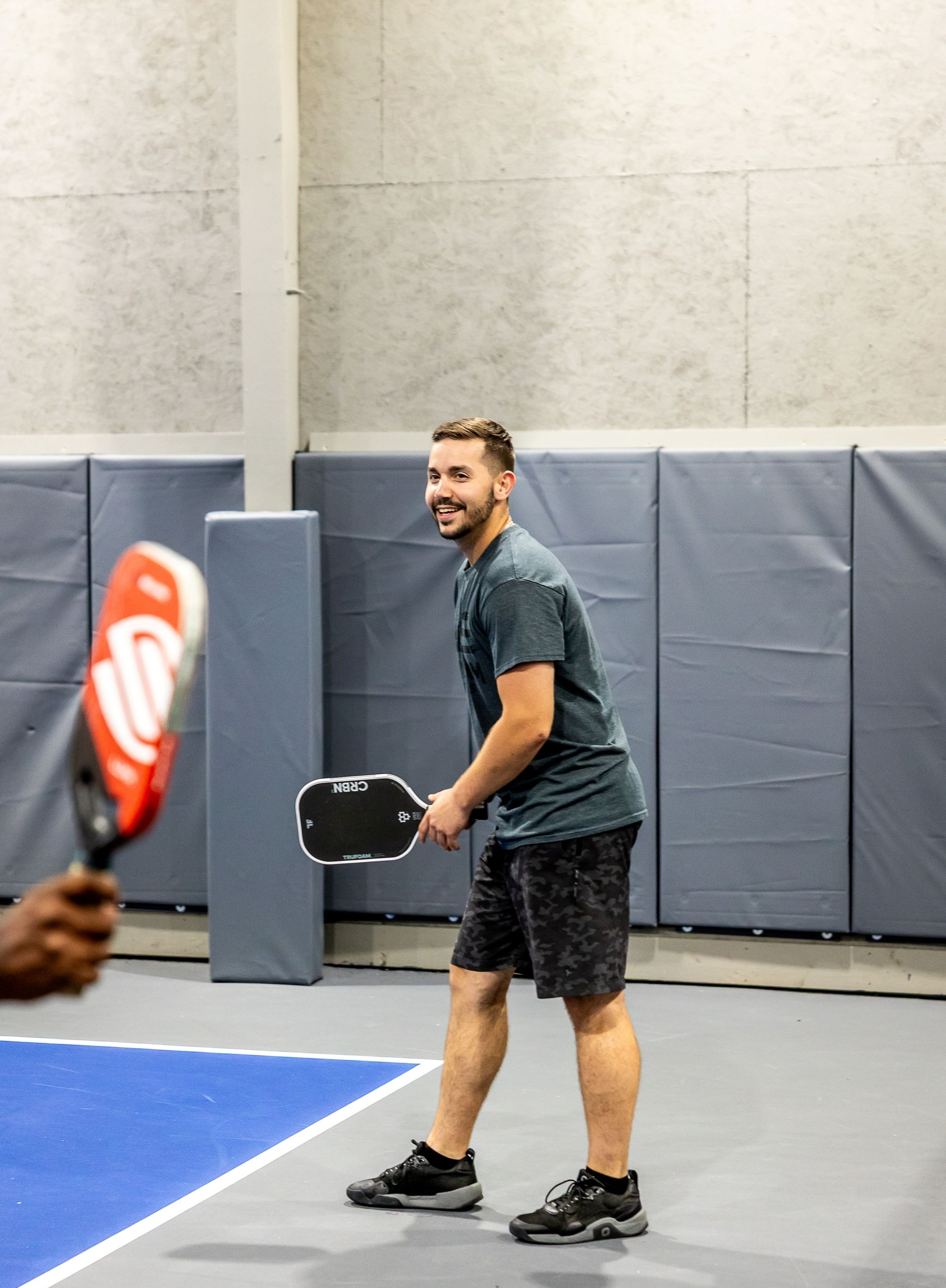 Smiling pickleball player getting ready to receive a shot on an indoor court.