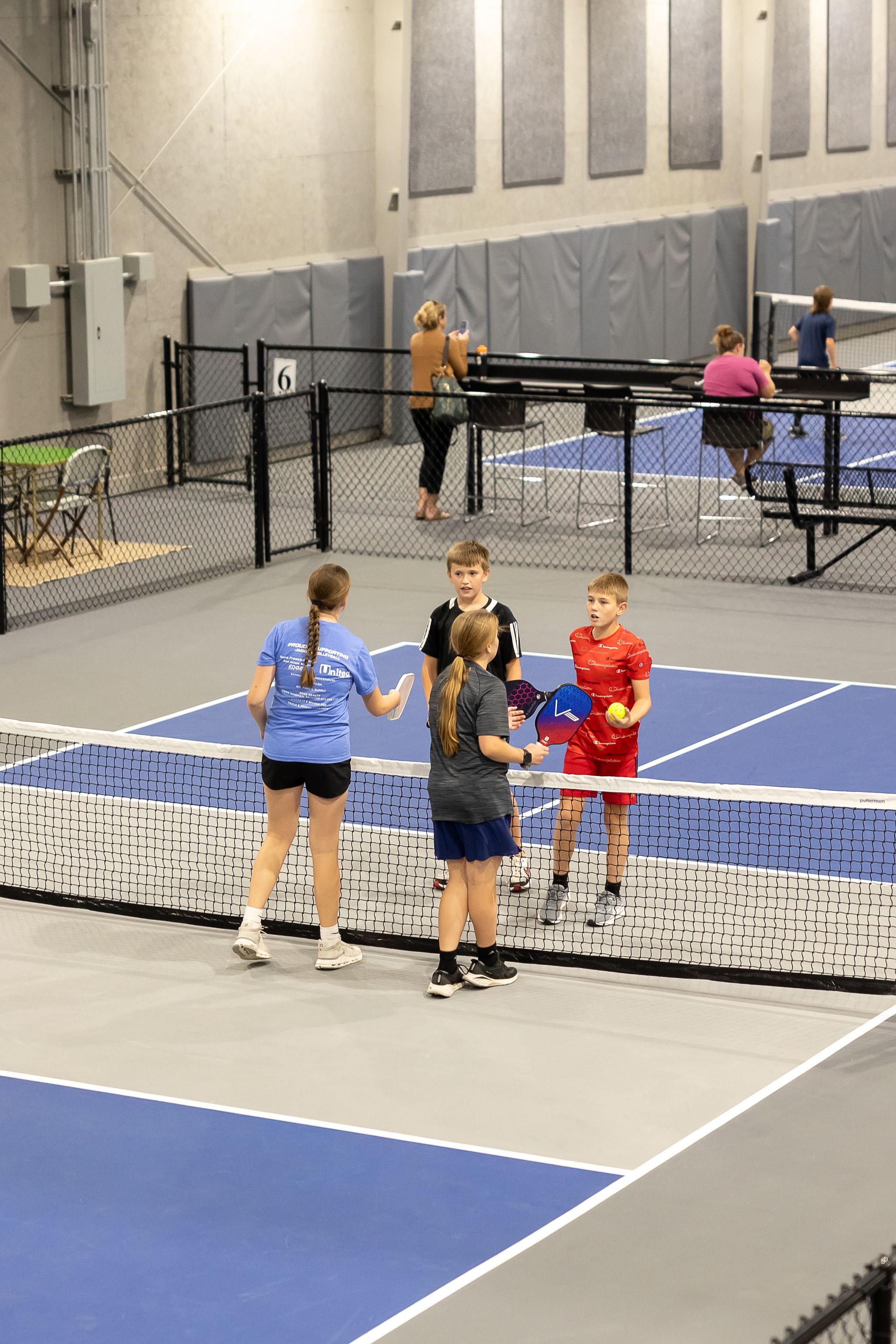 Kids tapping paddles at the net after a pickleball game on the indoor courts at Freedom Fitness