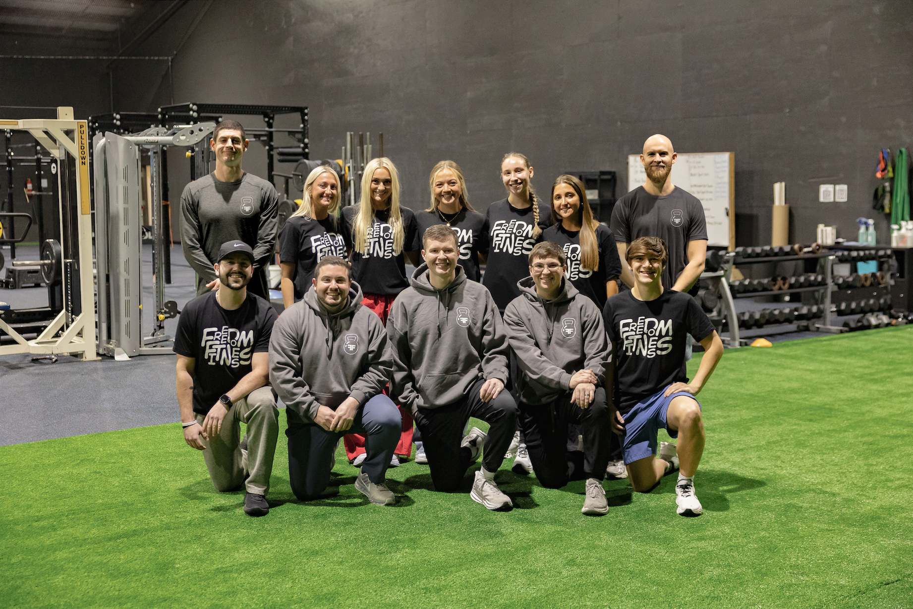 Group photo of the Freedom Fitness staff standing on the turf inside the gym facility