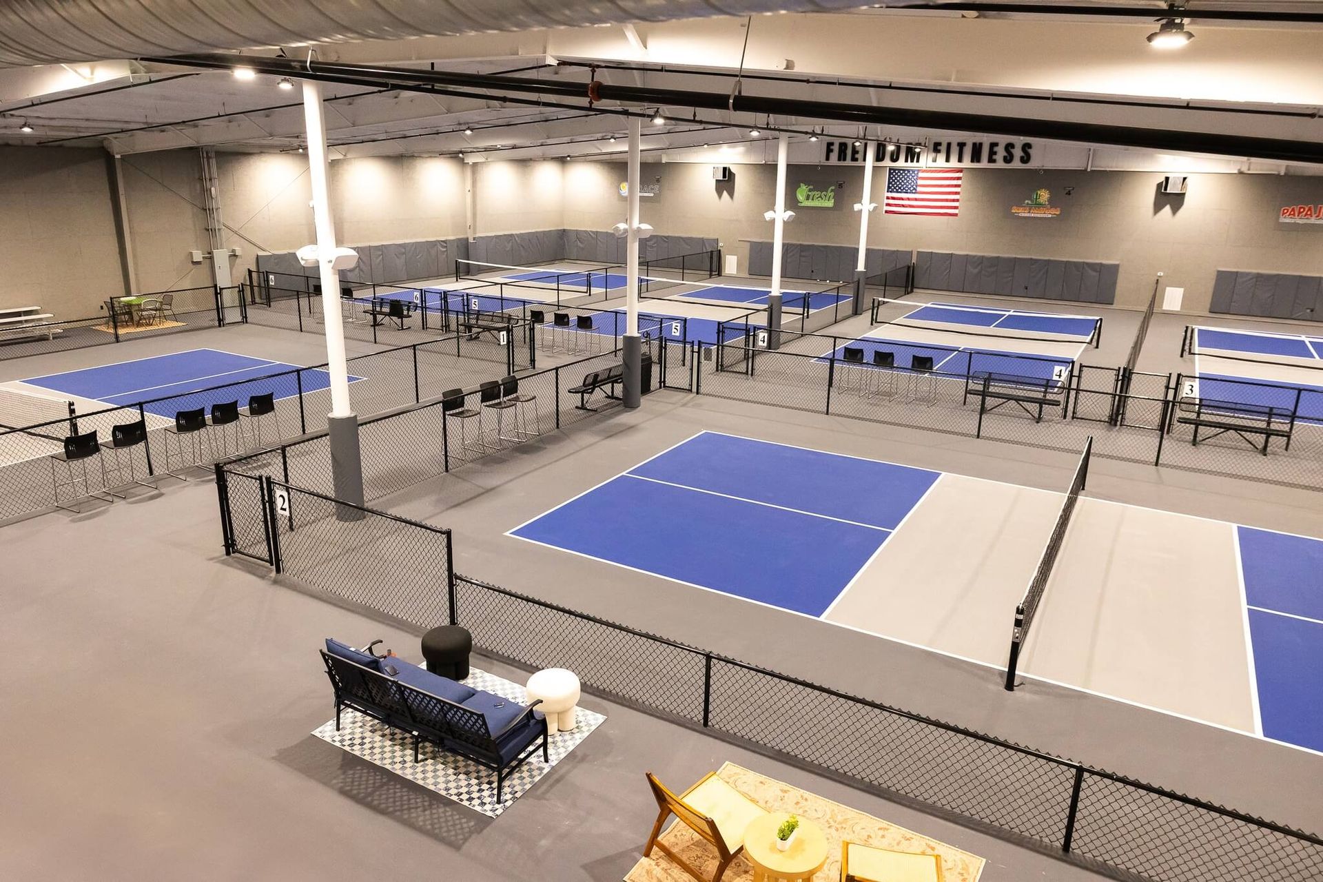 Spacious indoor pickleball complex at Freedom Fitness with fenced courts and comfortable seating areas.