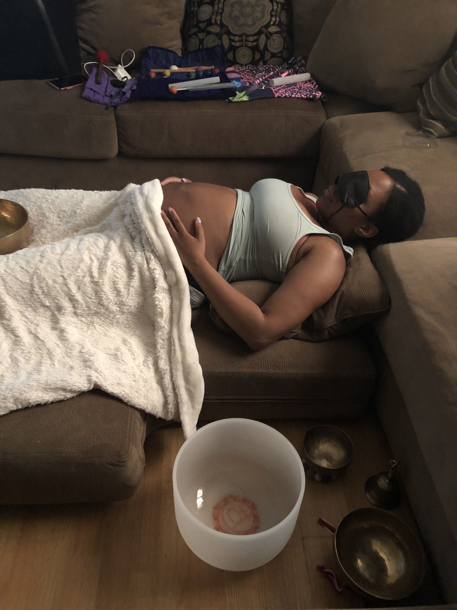 A pregnant woman is laying on a couch next to a bowl