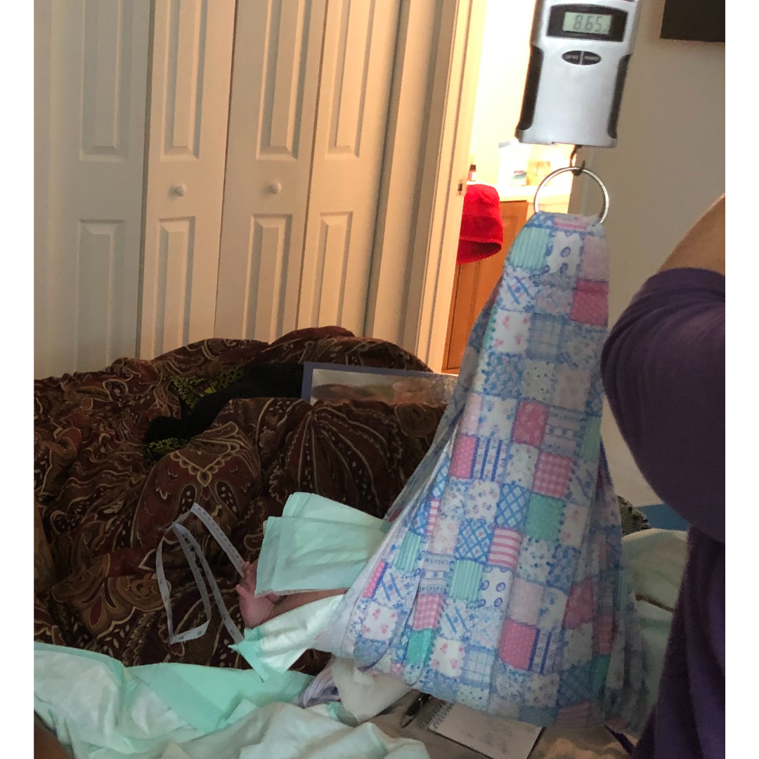 A baby in a sling is being weighed on a scale