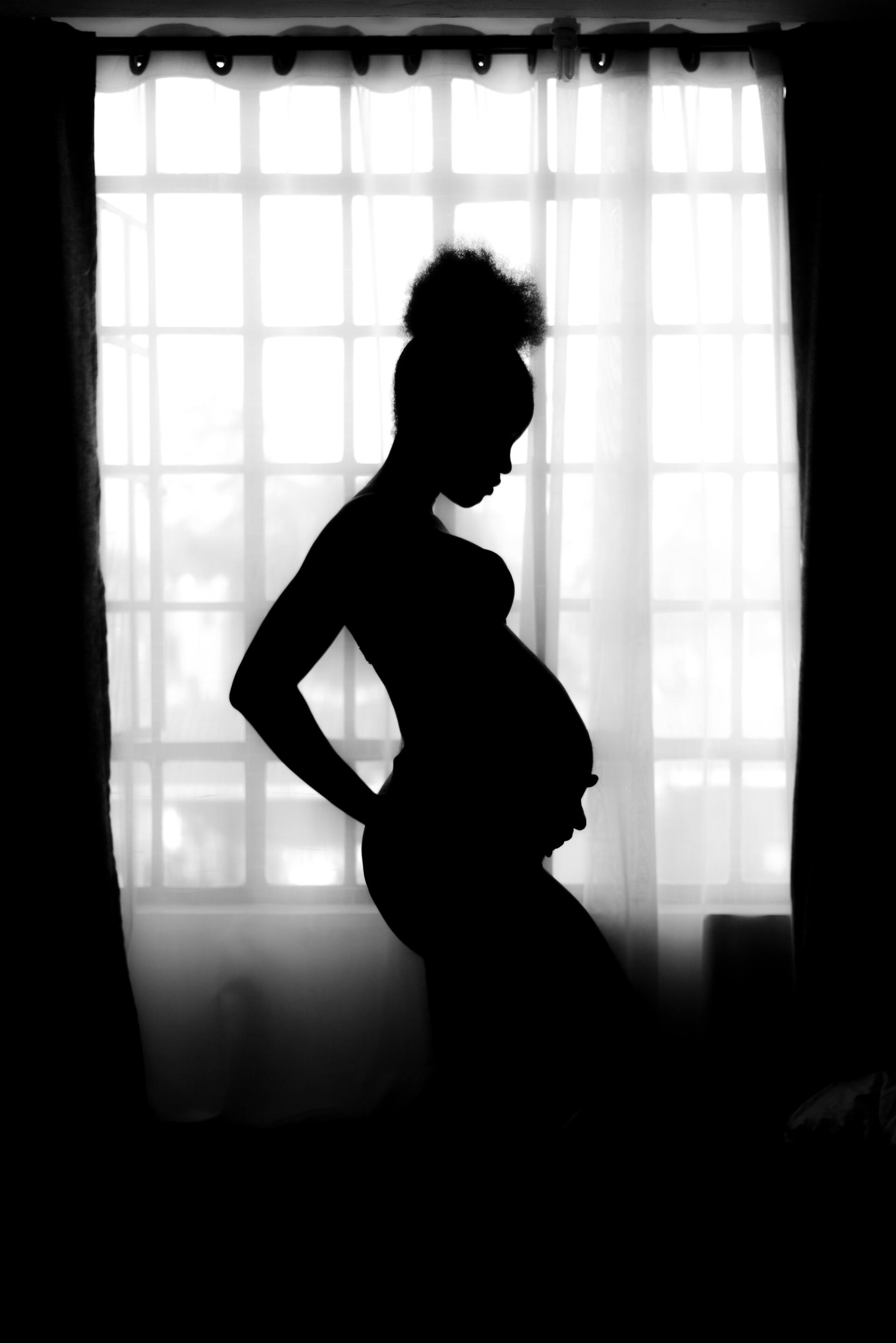 A silhouette of a pregnant woman standing in front of a window.