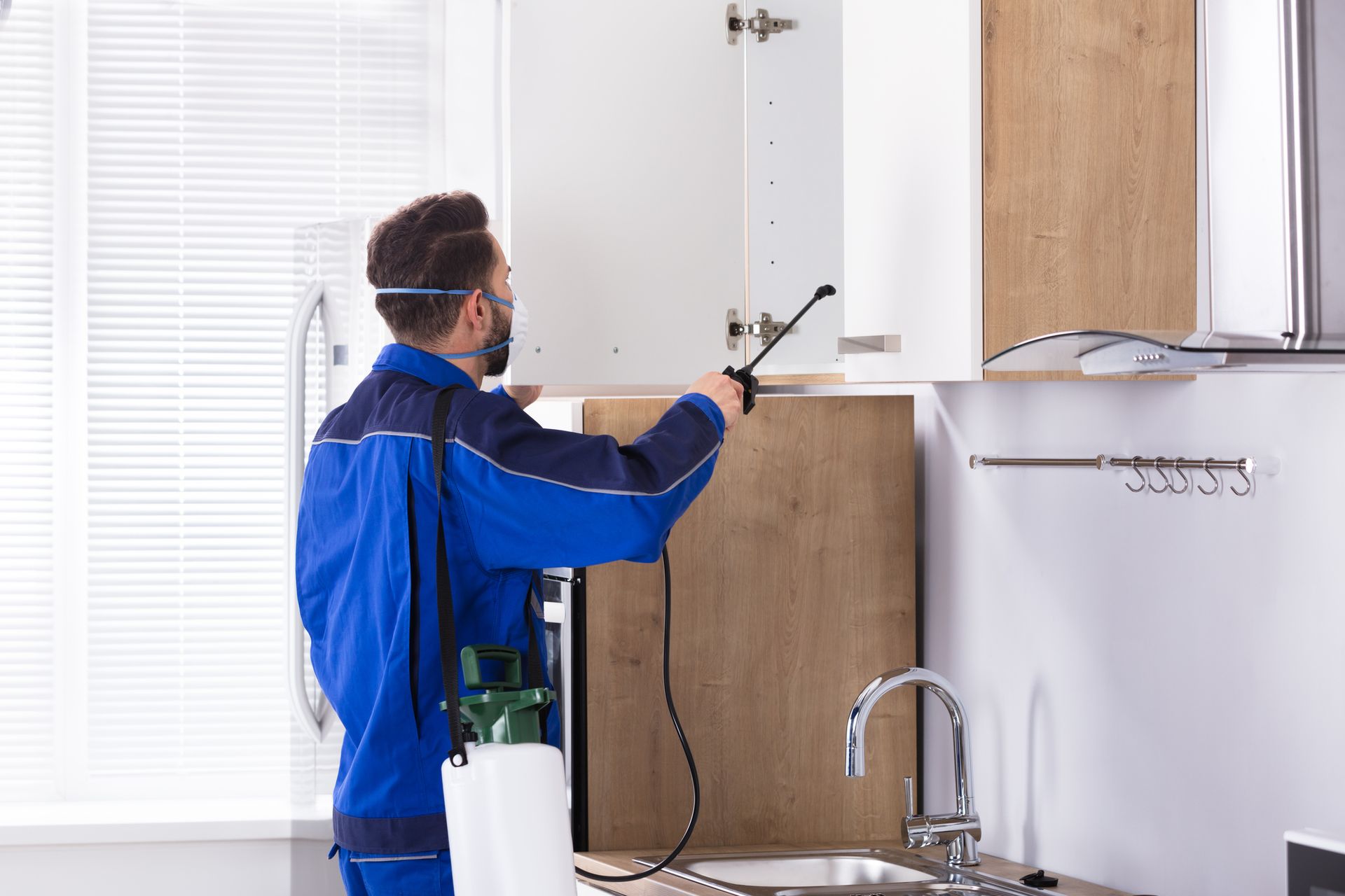 Technician in blue uniform performing a pest inspection service in a kitchen cabinet using a spray.