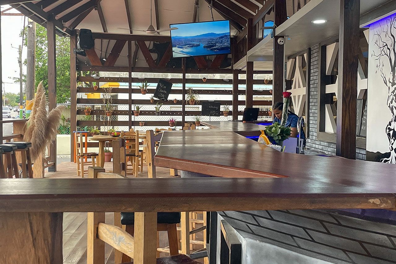 A restaurant with a long wooden table and stools and a television on the wall.
