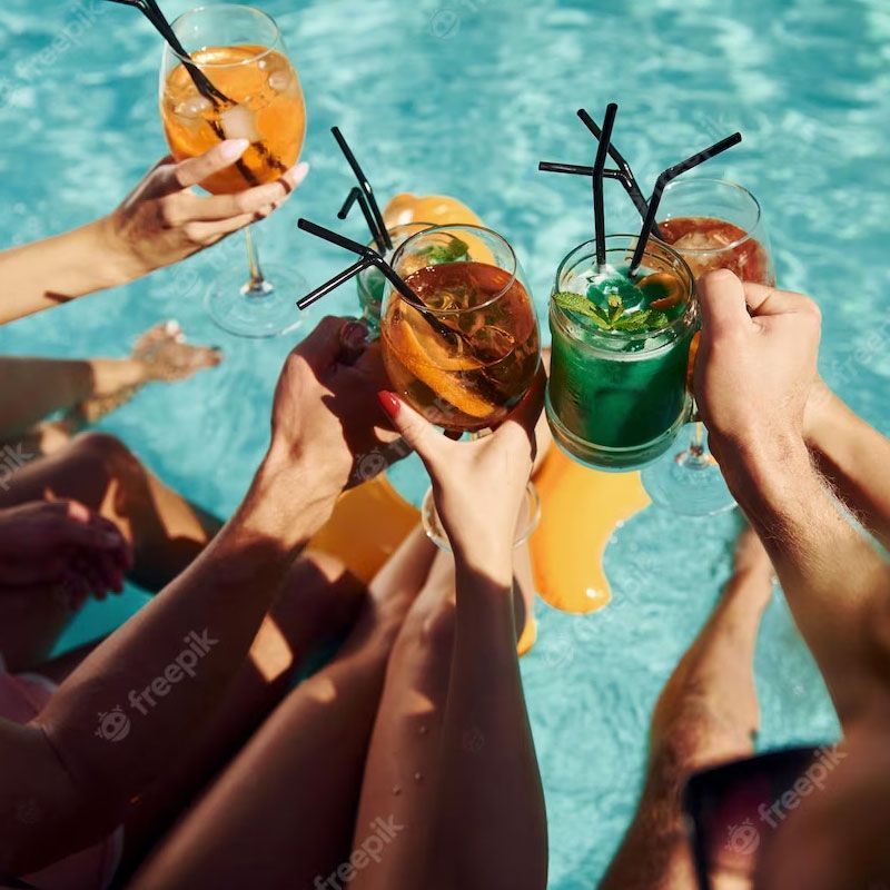 A group of people are toasting with drinks in a swimming pool.
