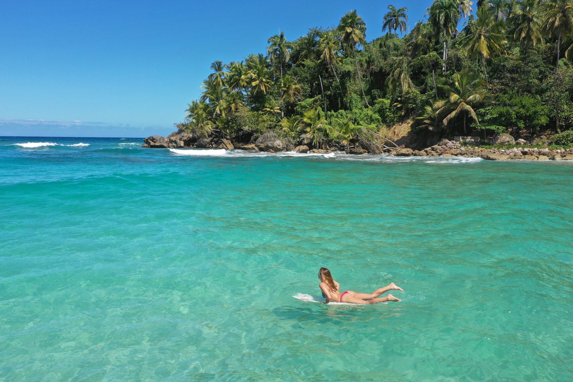 A woman is laying on a surfboard in the ocean