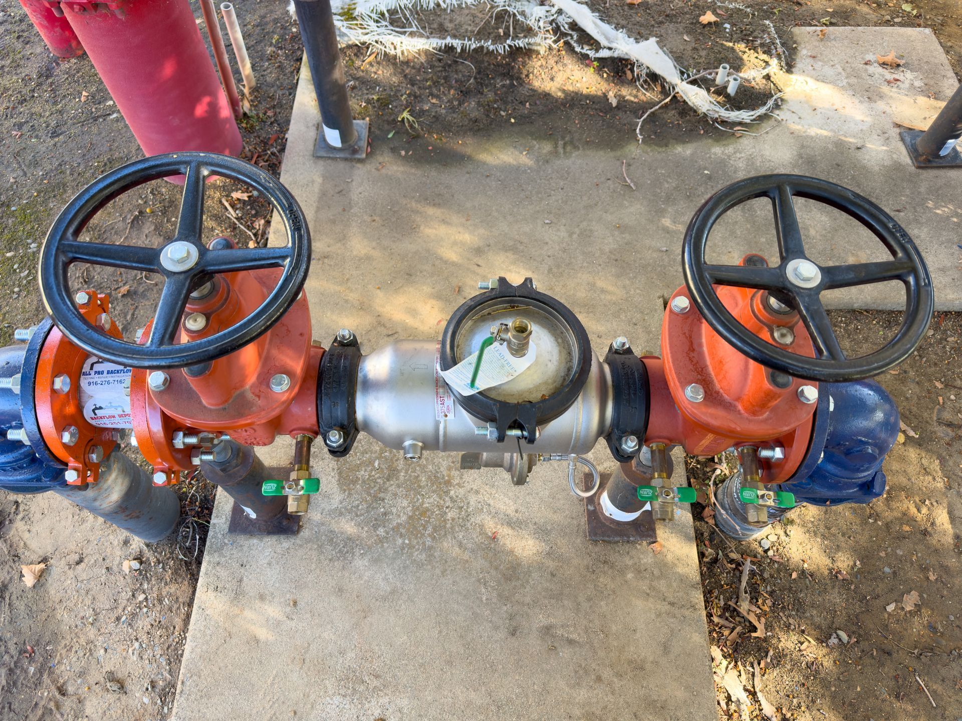 Water meter with two red valves and black handwheels, set on a concrete pad.