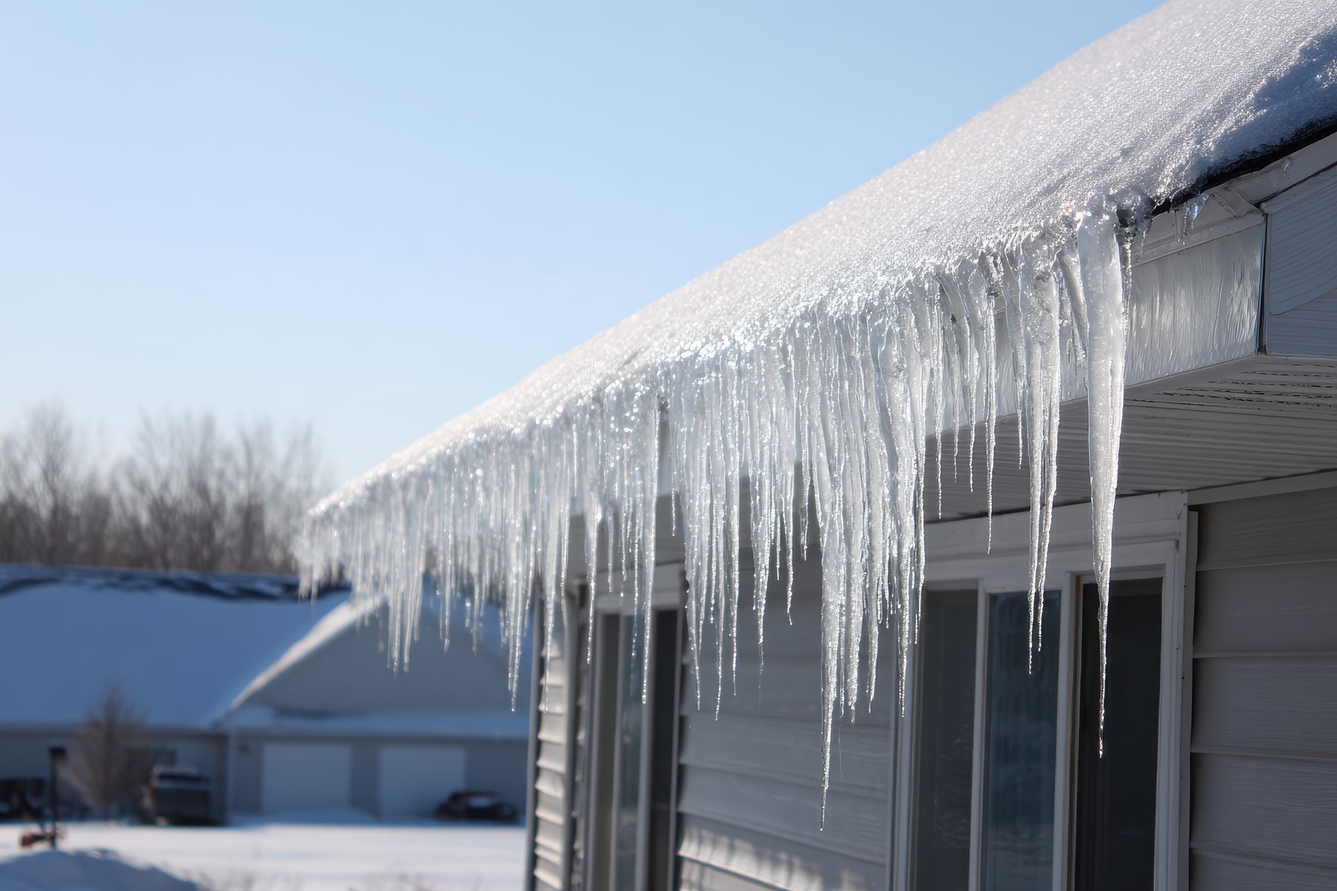 Icicles hanging from a roof in bright sunlight, snowy background.