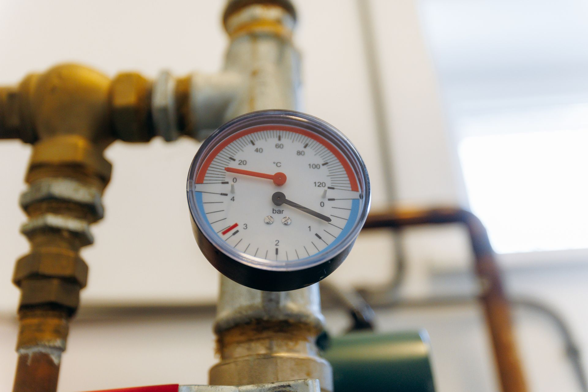 Close-up of a pressure gauge on a pipe with red and blue temperature indicators.