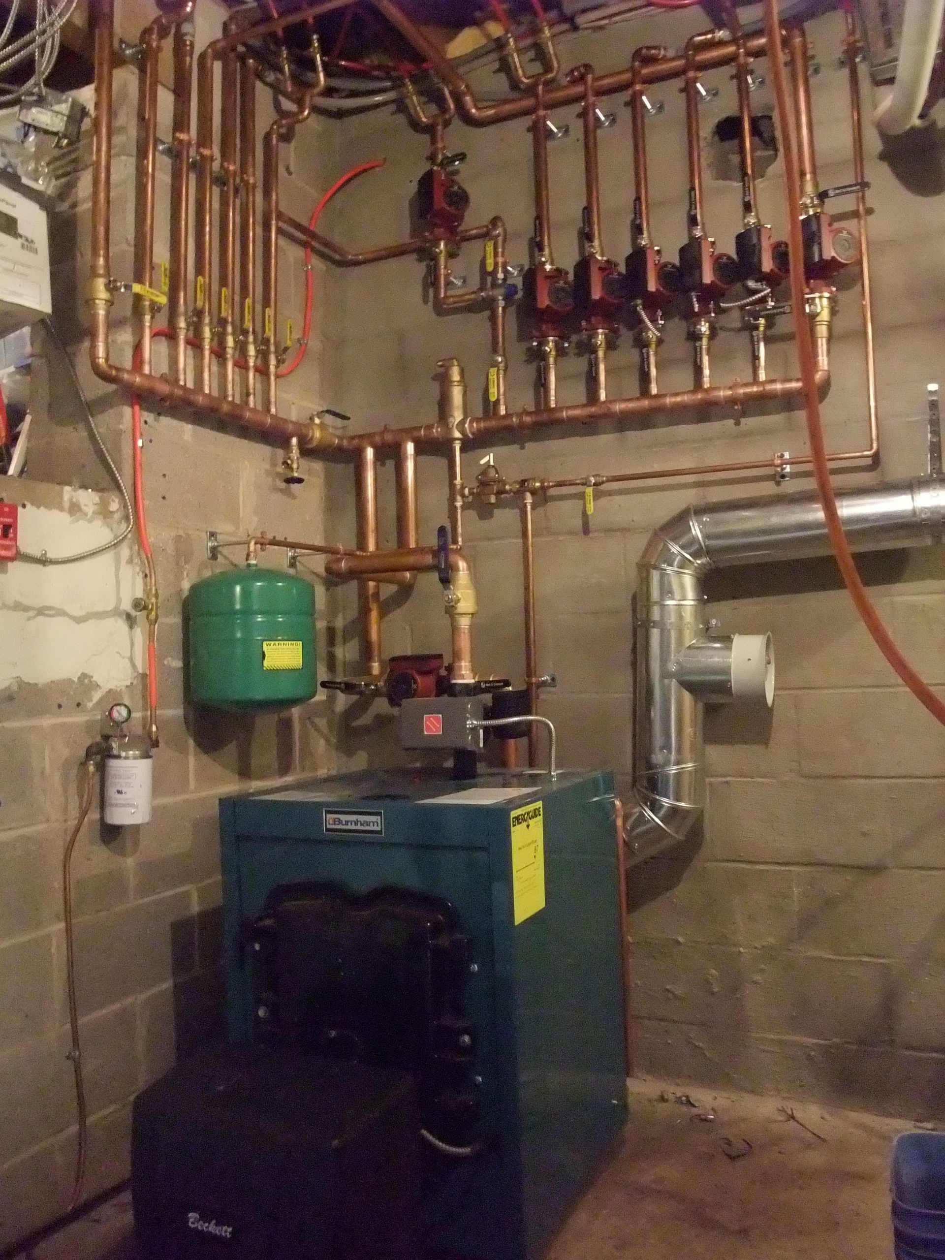 Copper pipes and valves for a boiler system on a basement wall.