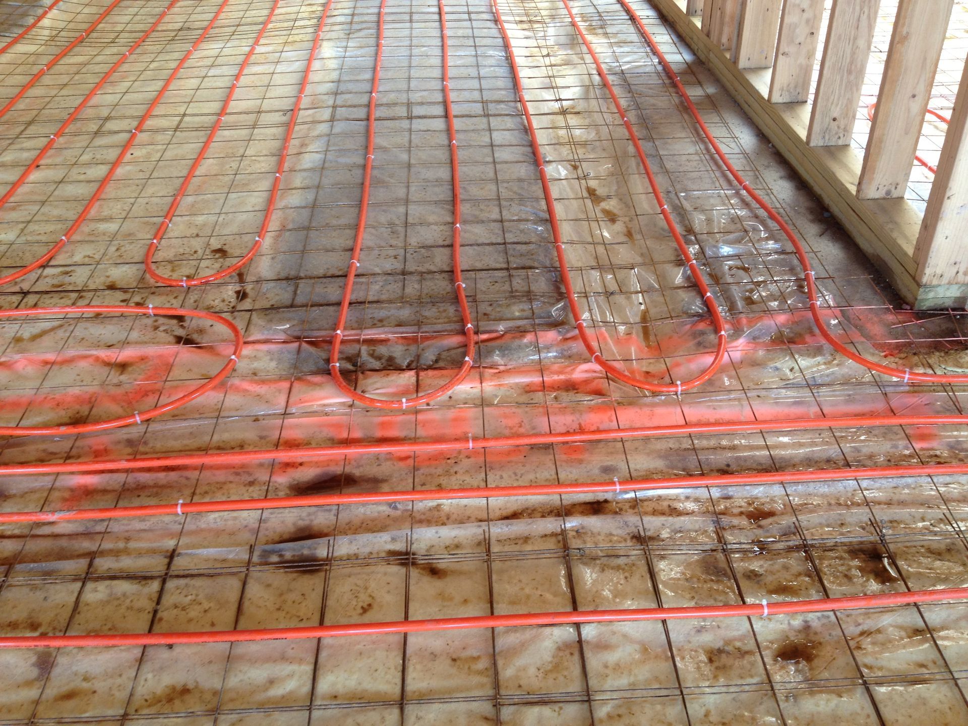 Orange radiant floor heating tubes laid on a wire mesh in a construction setting.