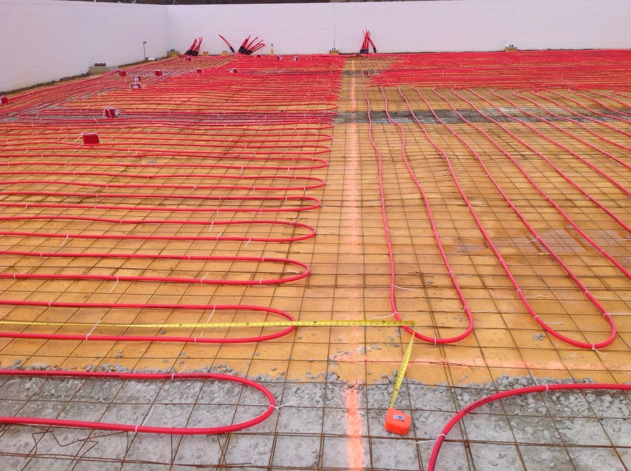 Red radiant floor heating tubes laid on concrete, ready for installation.