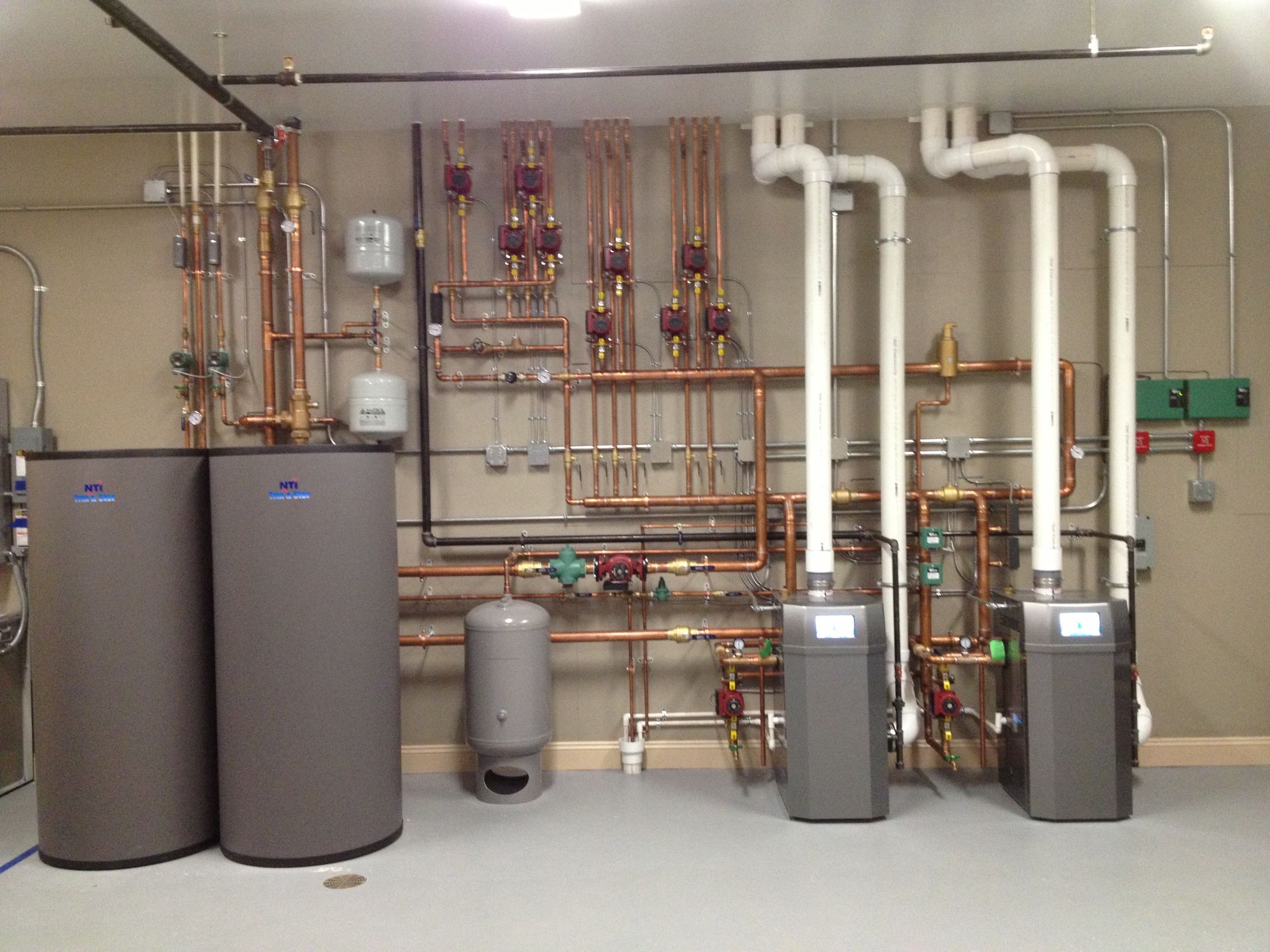 A complex plumbing system with tanks, pipes, and valves against a neutral wall.