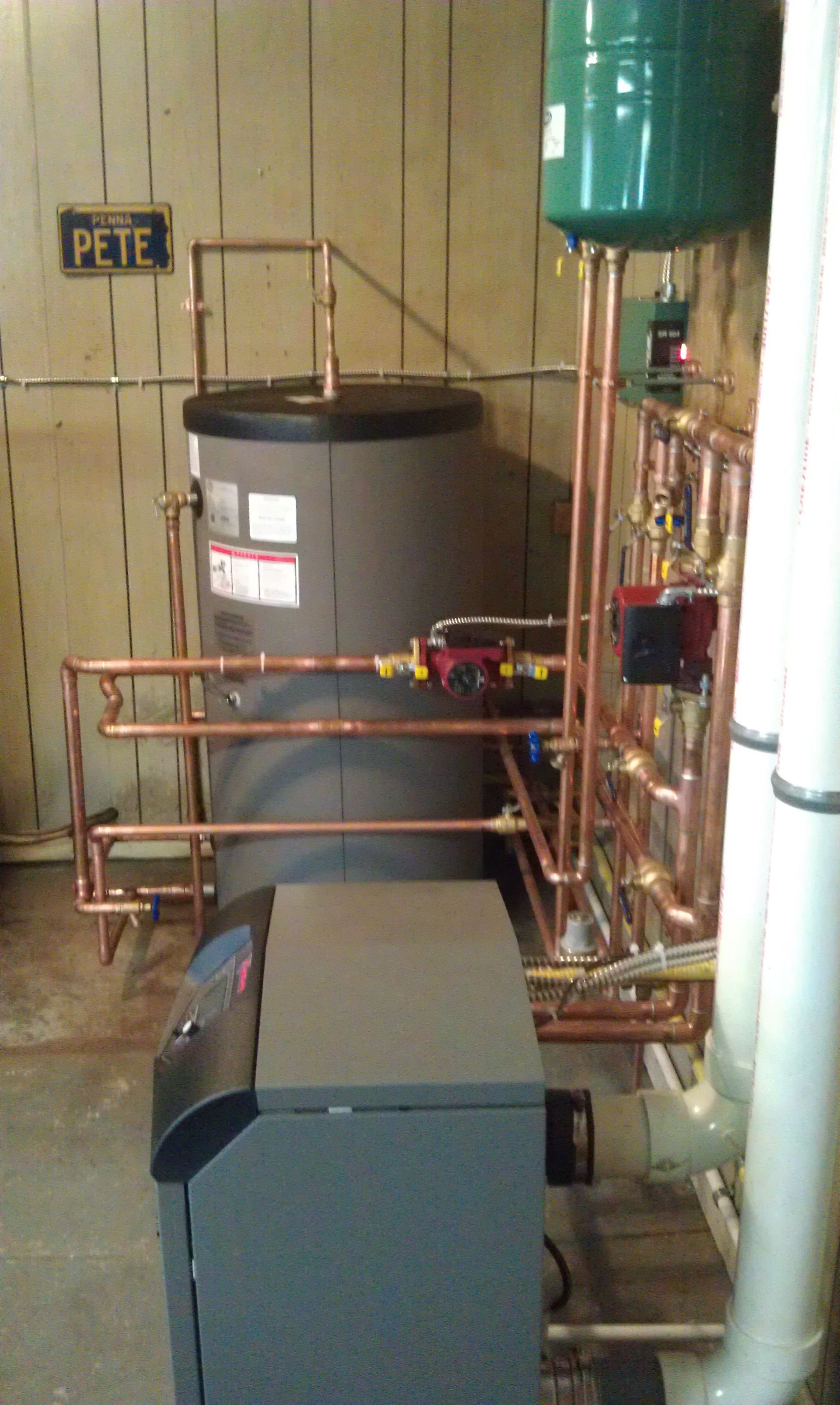 A water heater and associated copper pipes in a basement setting. A nameplate reads 