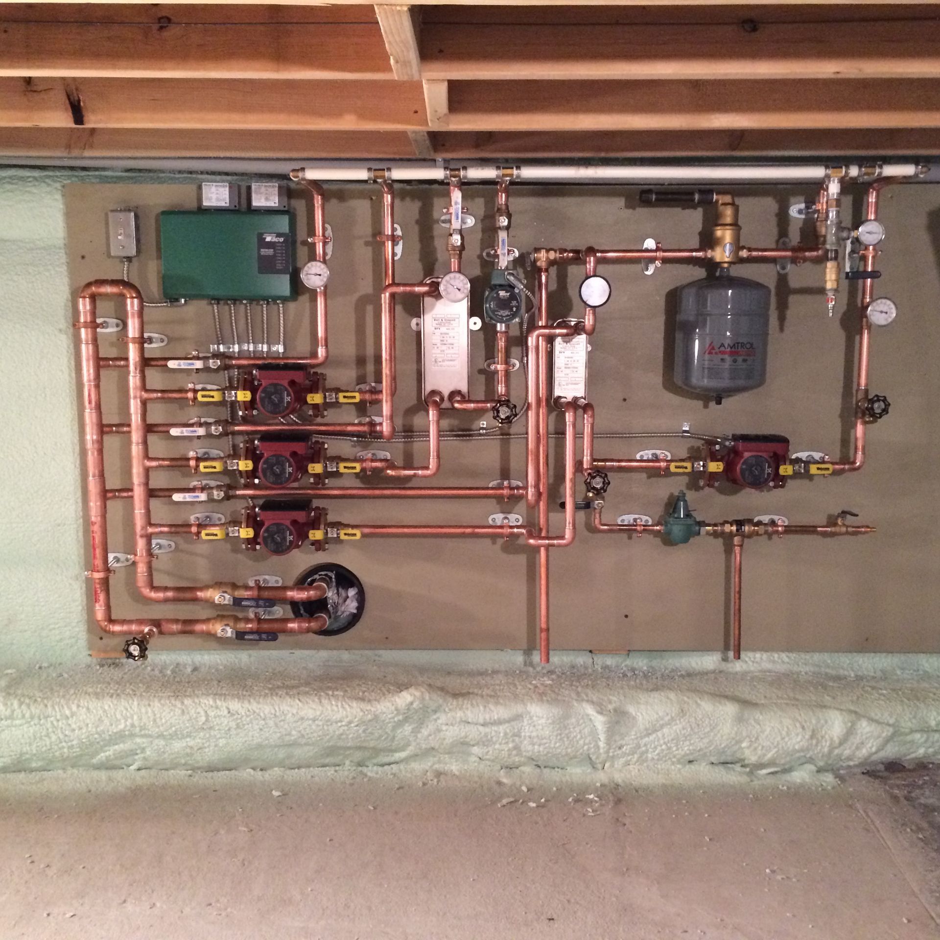 Copper pipes and heating equipment on a wooden board in a basement.