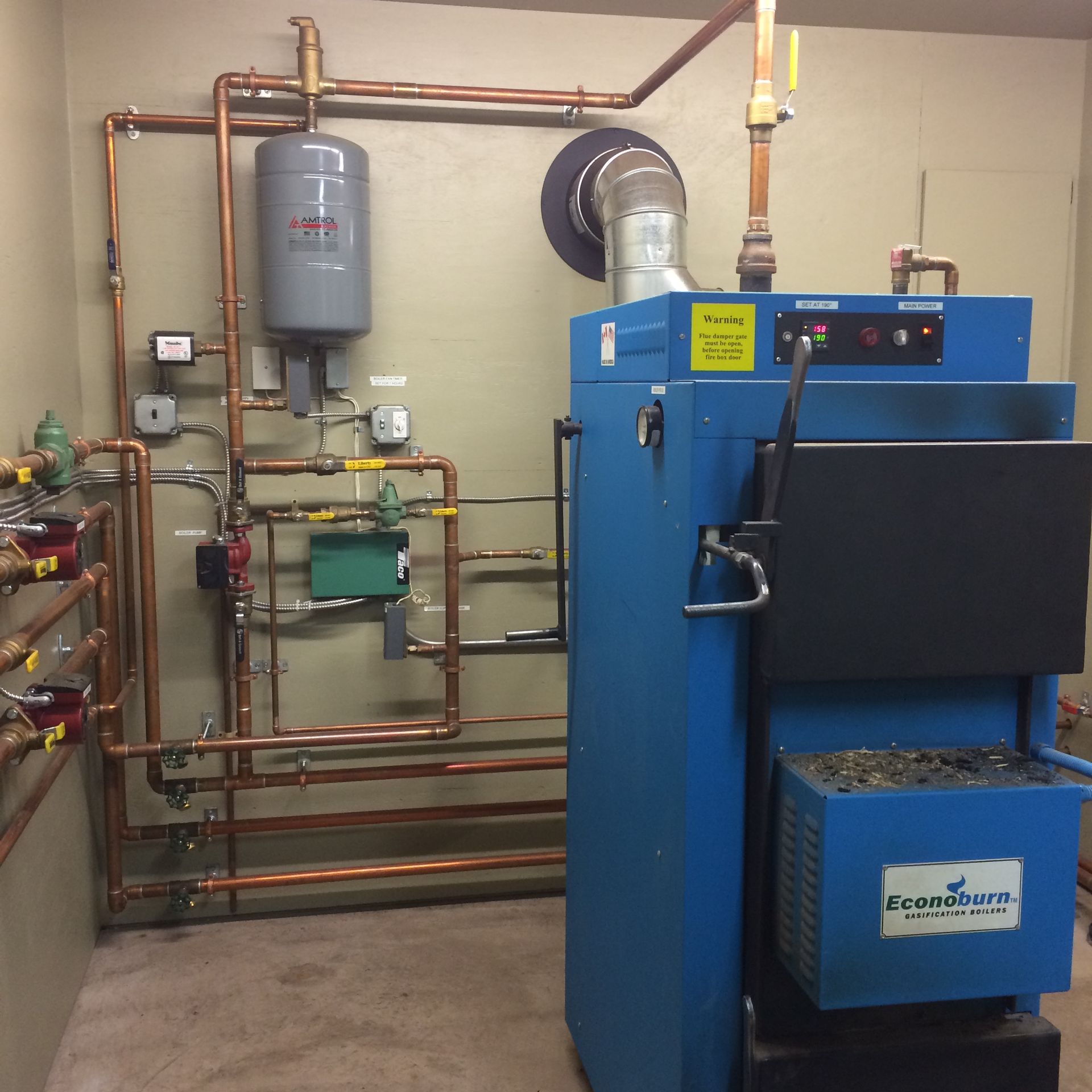 Blue boiler with copper pipes, tank, and controls in a utility room.