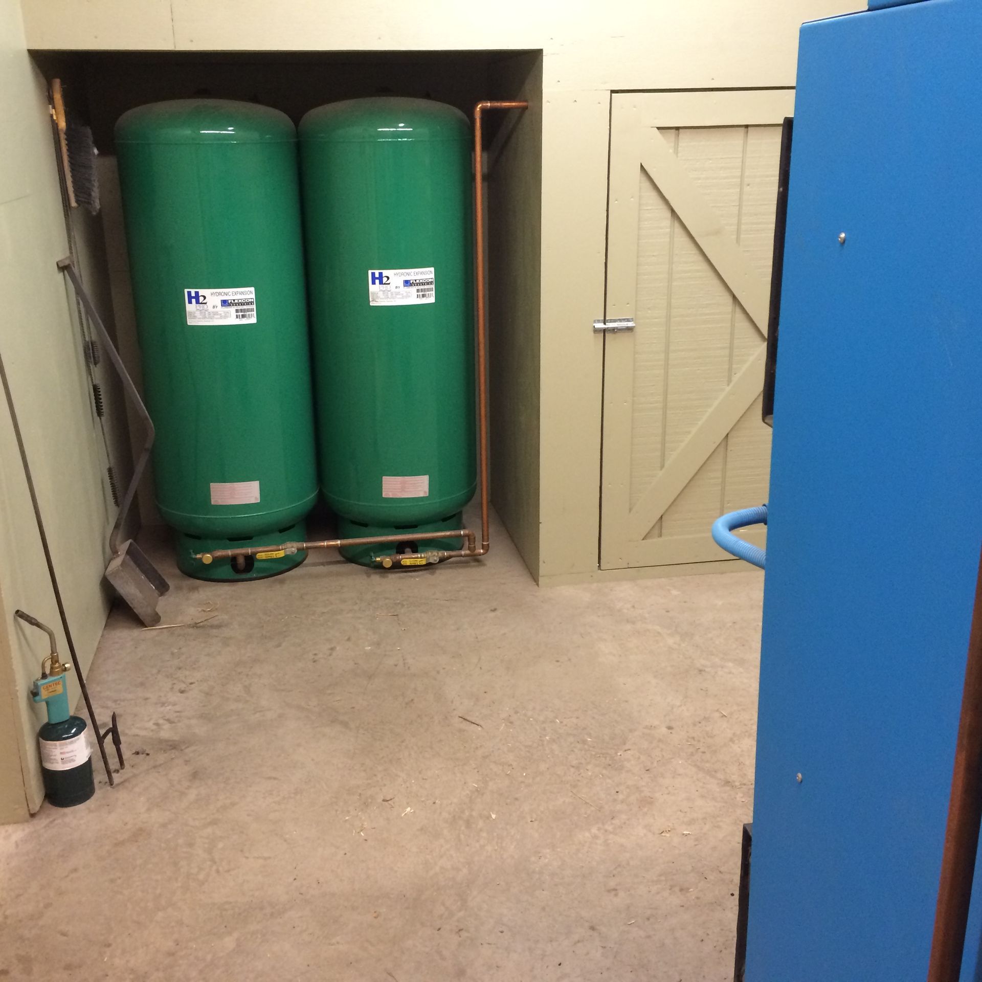 Two green water tanks and a blue appliance in a utility room with a closed door.