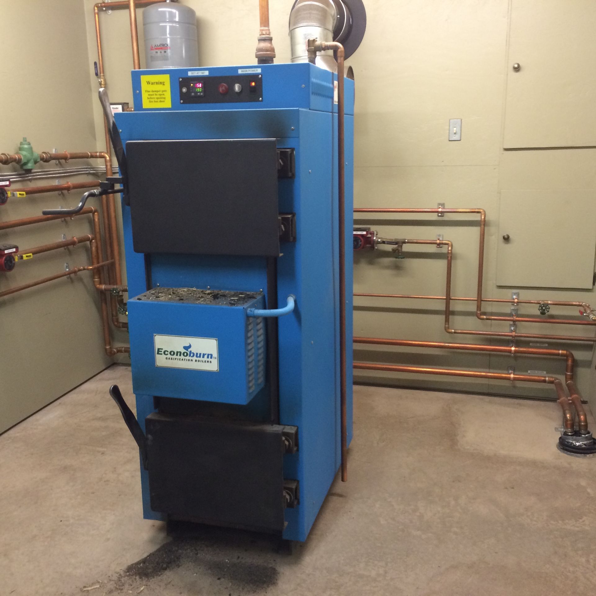 Blue wood-burning boiler with black doors and copper pipes in a utility room.