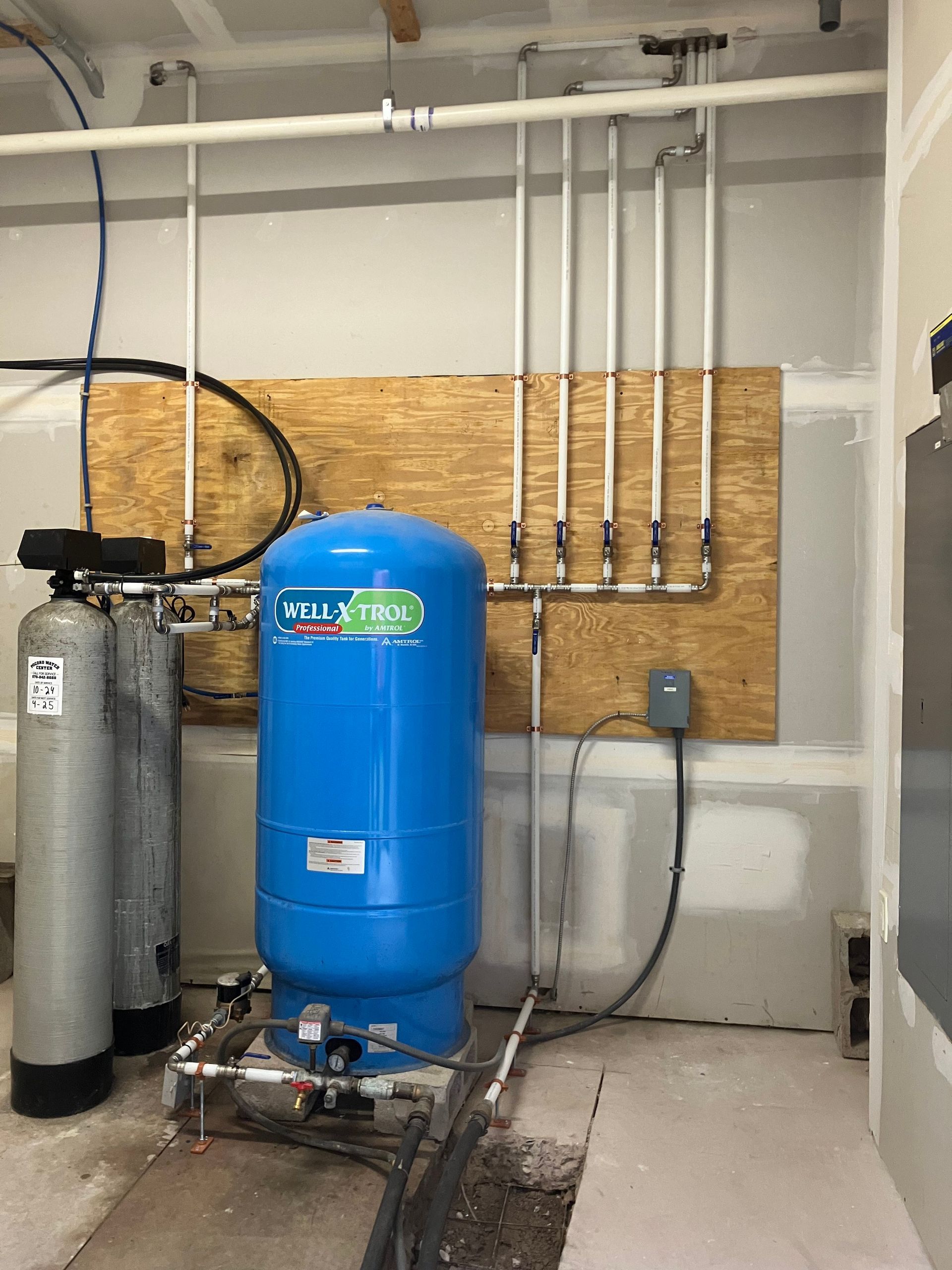 Blue water pressure tank and pipes in a utility room. Two cylindrical tanks are on the left.
