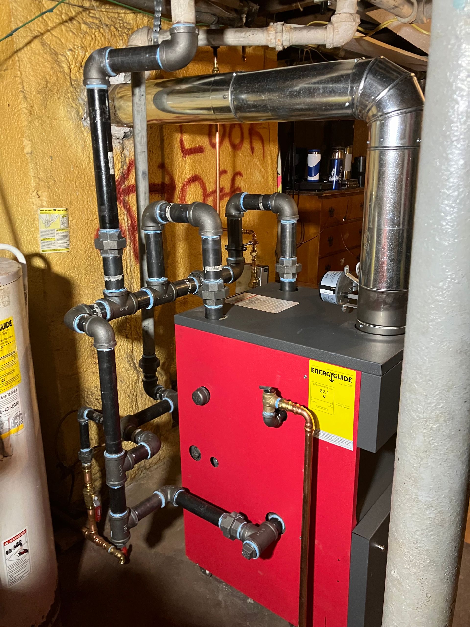Red boiler with black pipes in a basement setting.