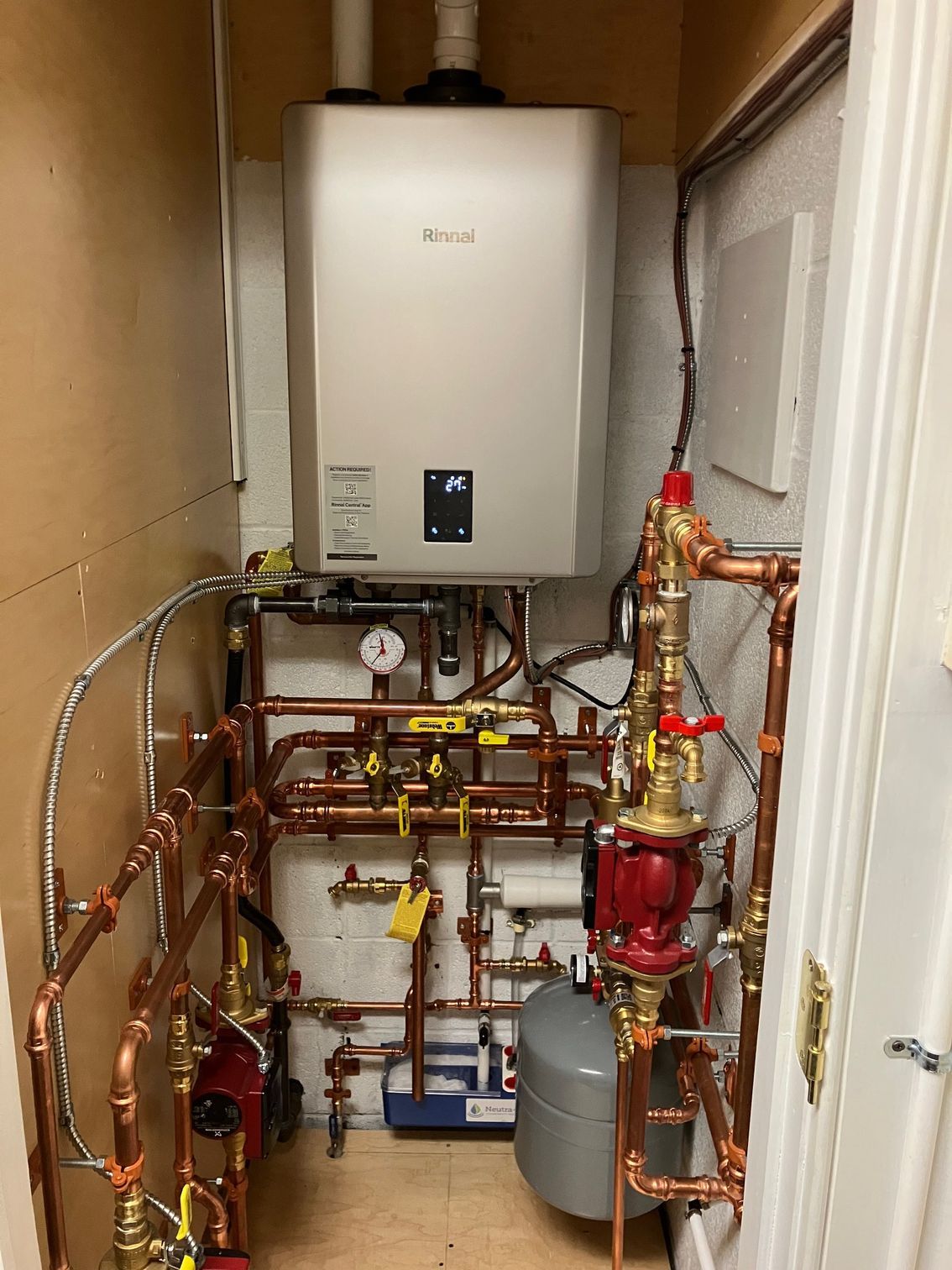 A water heater unit with copper pipes and valves installed in a narrow utility closet.