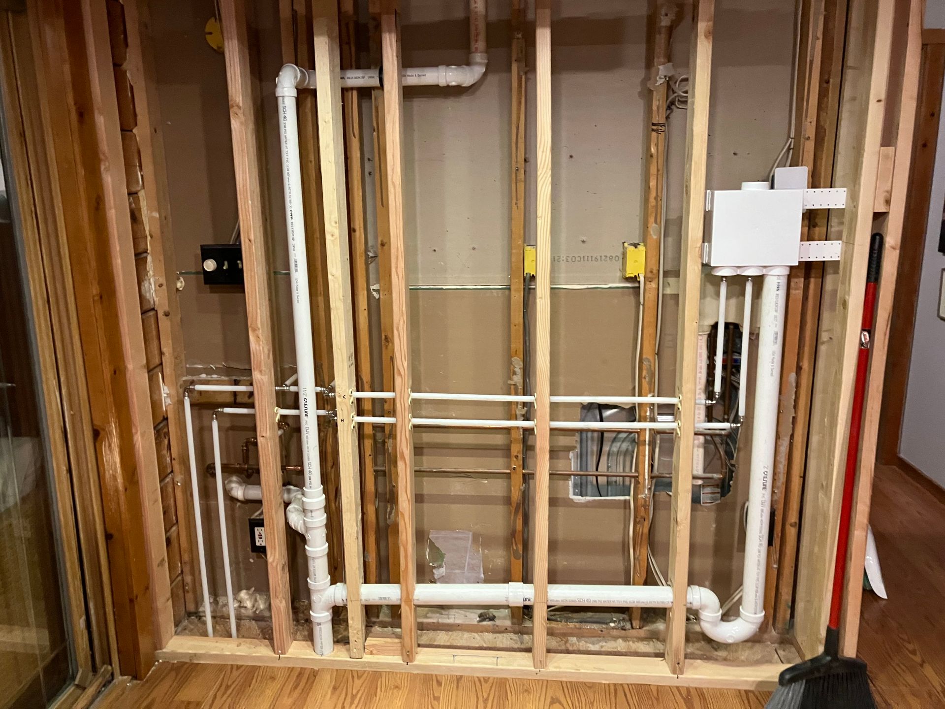 Interior wall framing with plumbing pipes visible; white PVC and copper, wooden studs.