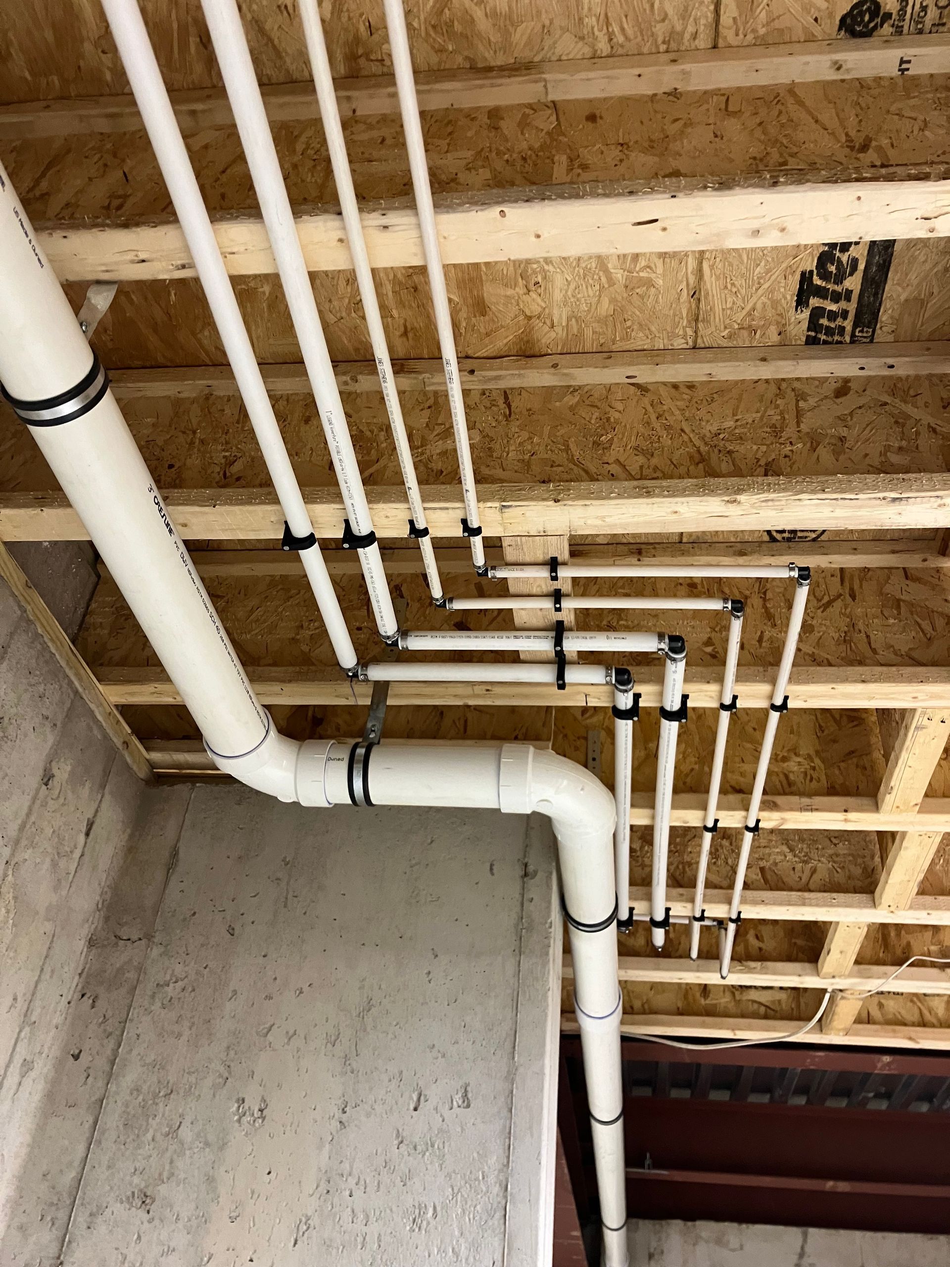 White PVC pipes installed on a wooden ceiling, connected with black clips, inside a concrete wall structure.