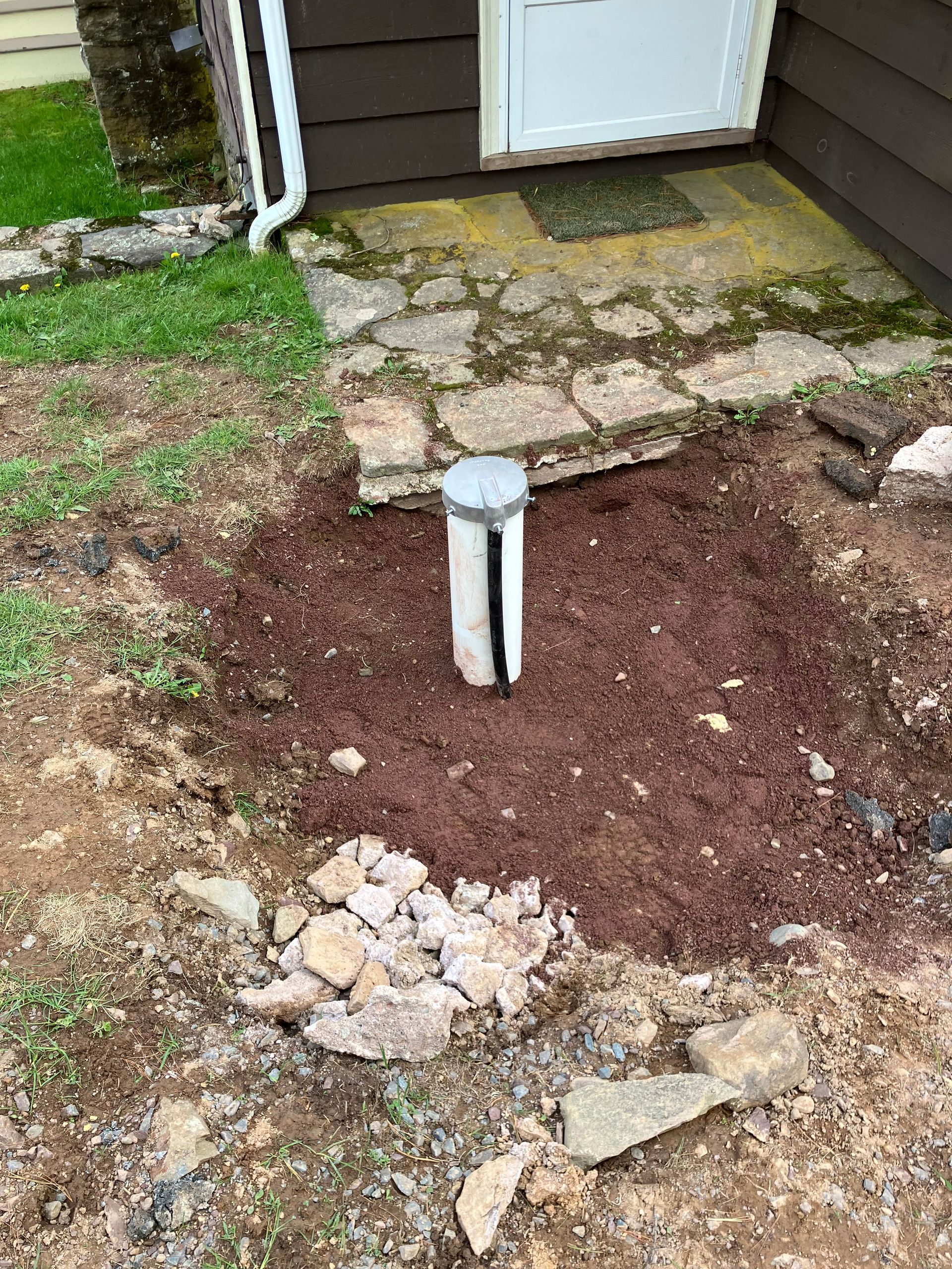 Gravely area with a white pipe. Dirt and small stones surround it near a door.