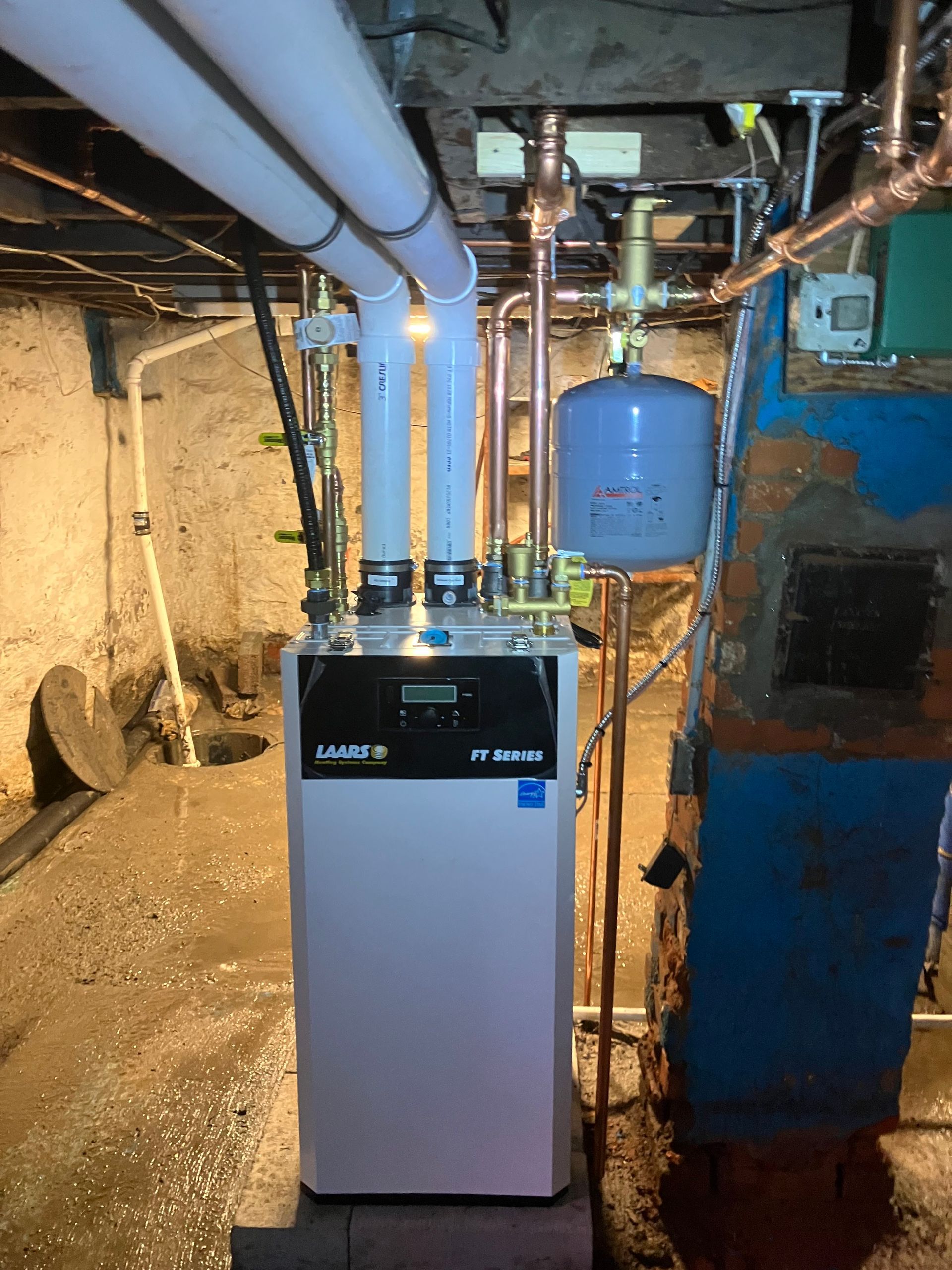 A modern white furnace with copper pipes in a basement setting.